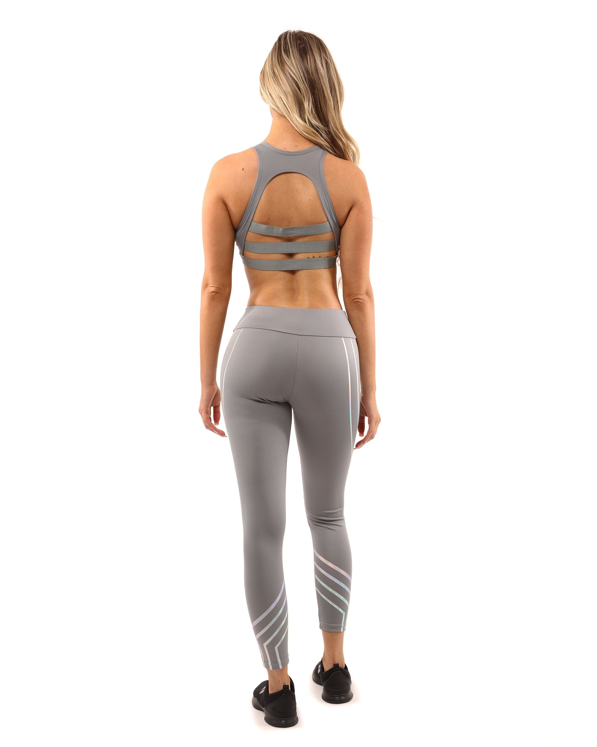 A person stands on a plain white background wearing the Laguna Set - Leggings & Sports Bra in grey, featuring geometric patterns.
