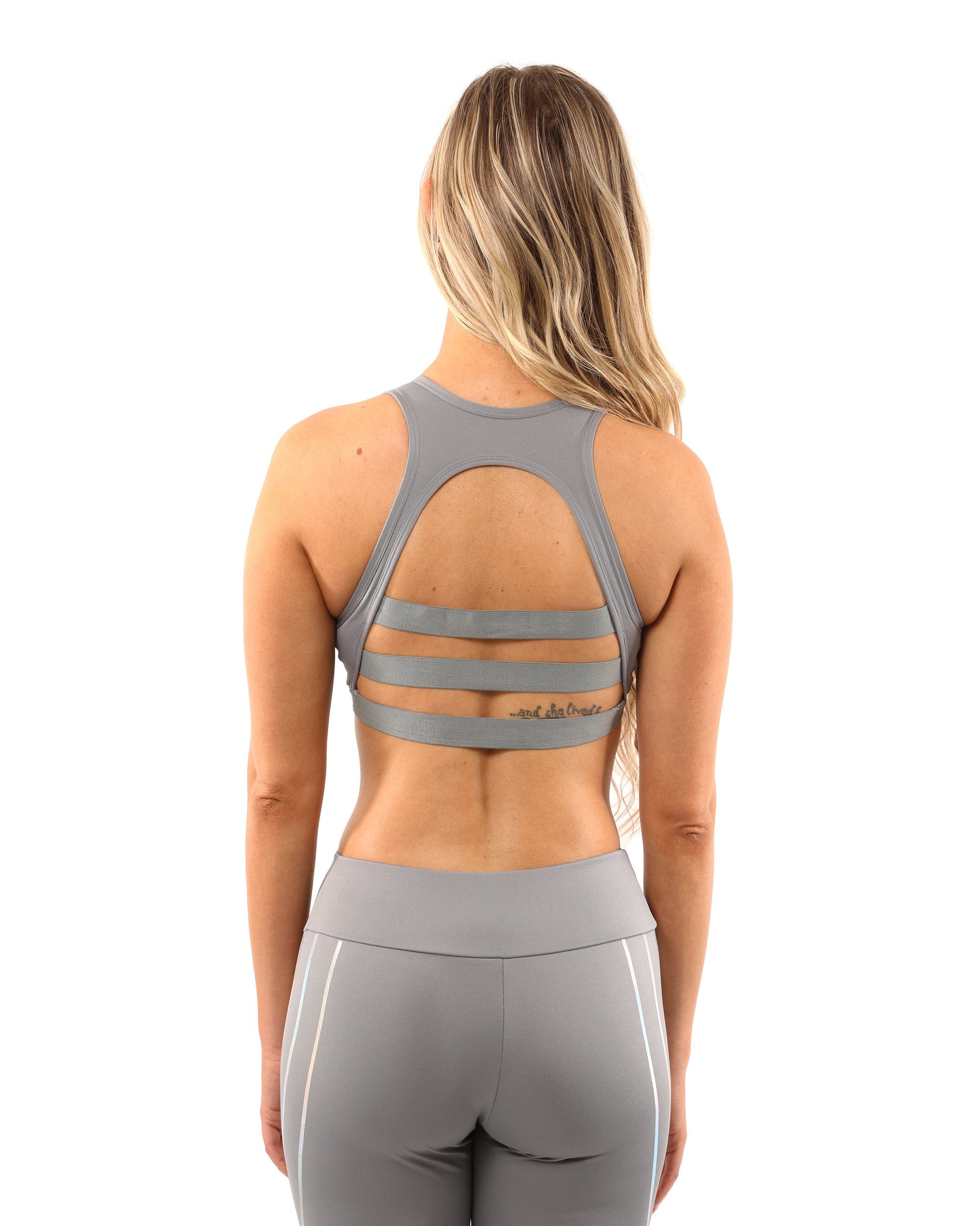 A person stands on a plain white background wearing the Laguna Set - Leggings & Sports Bra in grey, featuring geometric patterns.
