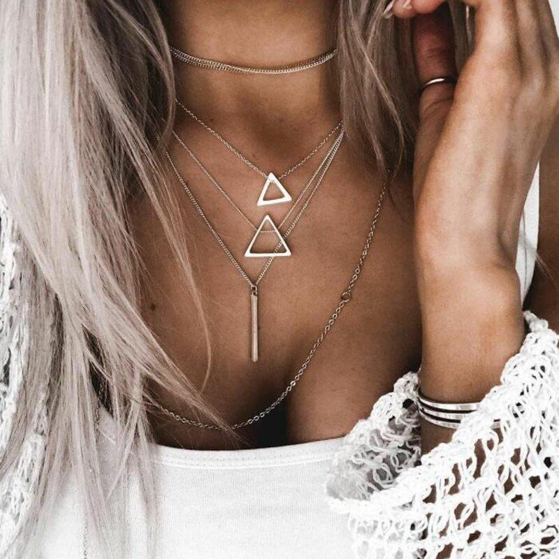A person with long hair wears a stunning Double Triangle Multilayer Necklace, featuring zinc alloy with an adjustable chain and geometric shapes. Complementing their look is a textured sleeve and a bracelet on their wrist.