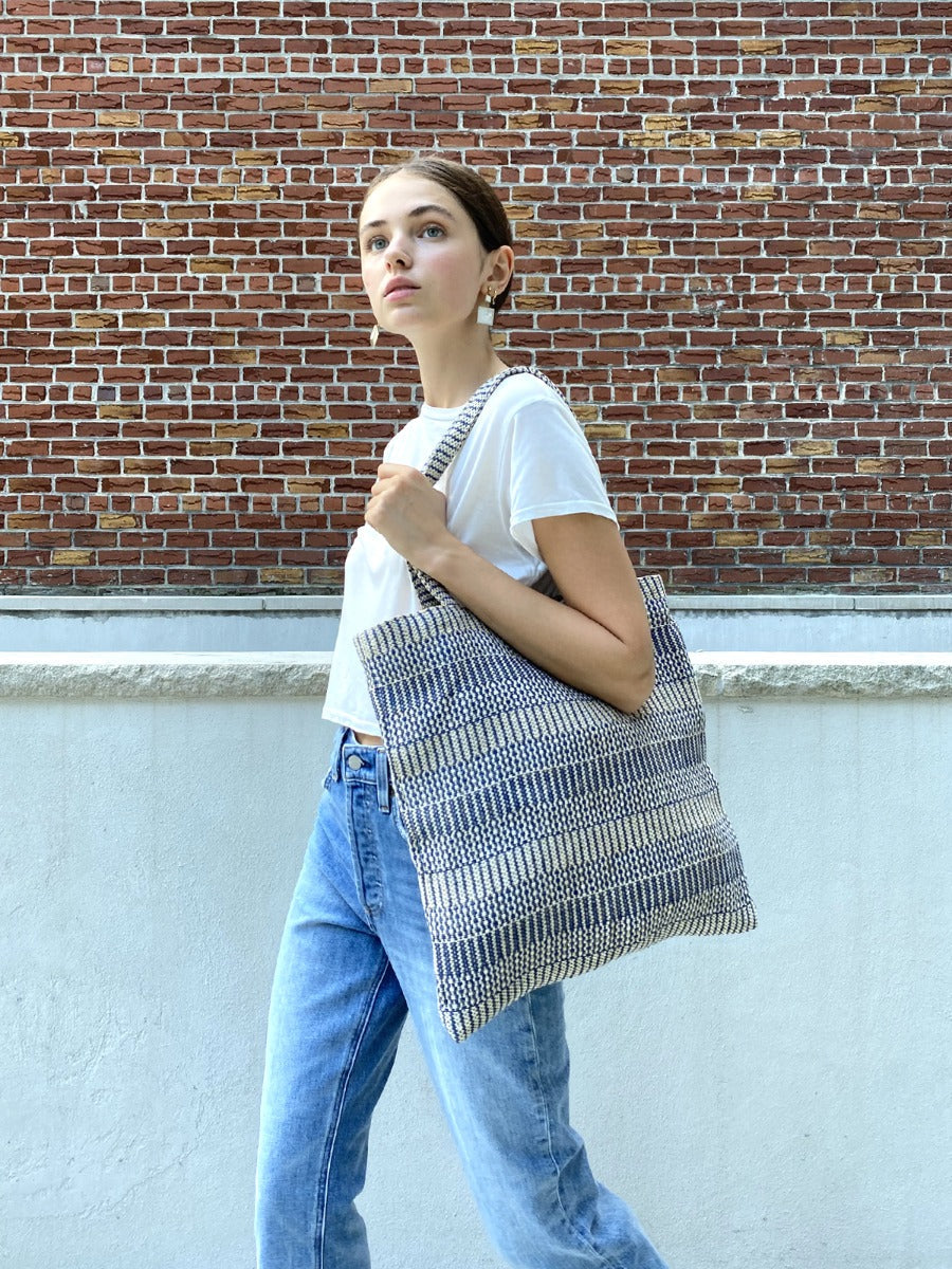 The Dobi Daily Bag - Blue is a tote bag crafted from handwoven jute-cotton fabric by Fair Trade artisans, featuring two handles set against a plain background, with gray and white horizontal stripes.