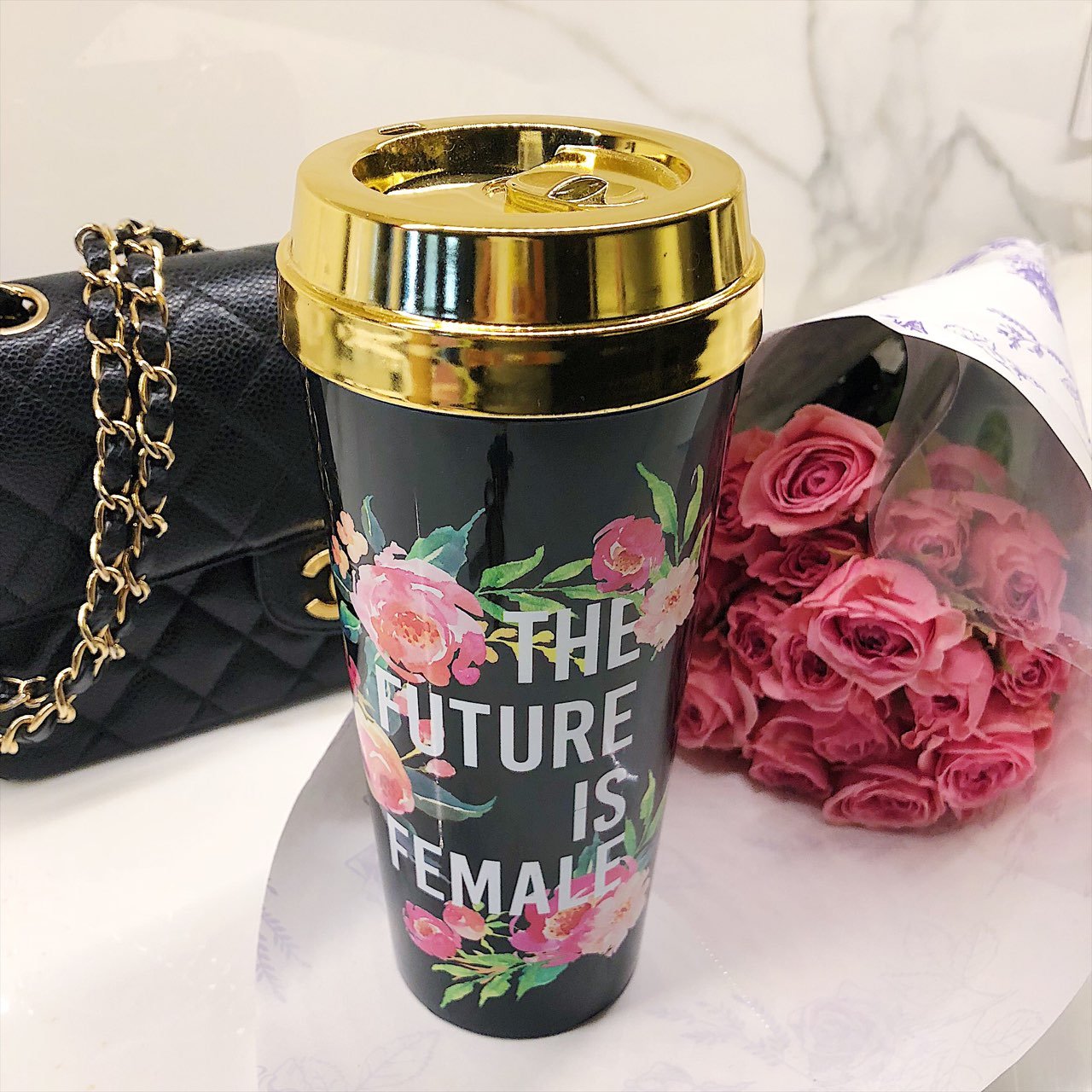 The travel mug, named "The Future Is Female," features elegant floral designs with a black body and a gold lid, prominently displaying the bold white phrase "The Future is Female," making it an ideal choice for those who support girl power and feminism.