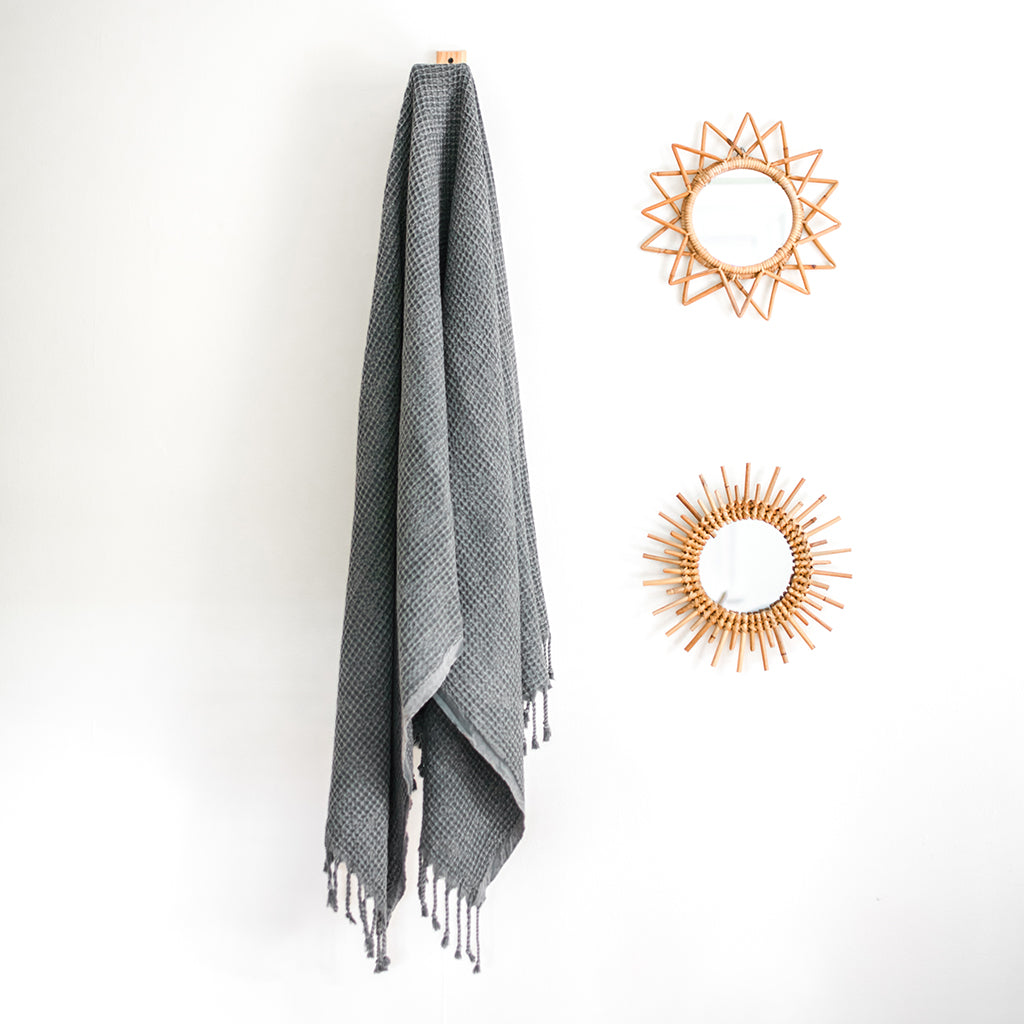 A folded, light gray blanket featuring a waffle texture and fringe tassels at the bottom mirrors the elegance of the Waffle Weave Turkish Towel, combining style and practicality for any cozy setting.