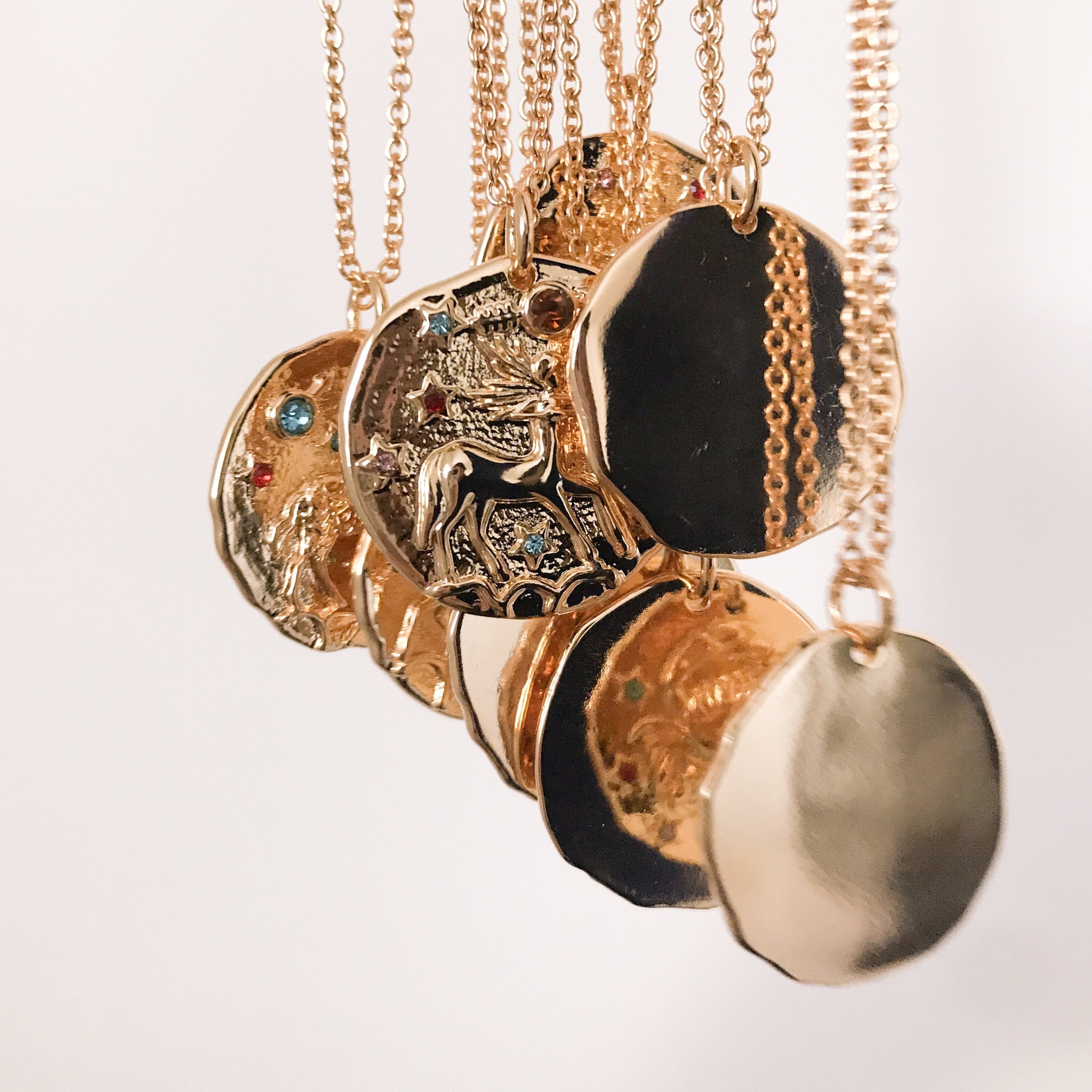 Discover our Wanderlust Zodiac Necklace collection, featuring exquisite hanging gold pendants with intricate designs on delicate chains. Some necklaces are embellished with vibrant gemstones. Crafted with hypoallergenic 18K gold plating, these pieces effortlessly combine elegance and comfort for everyday wear.