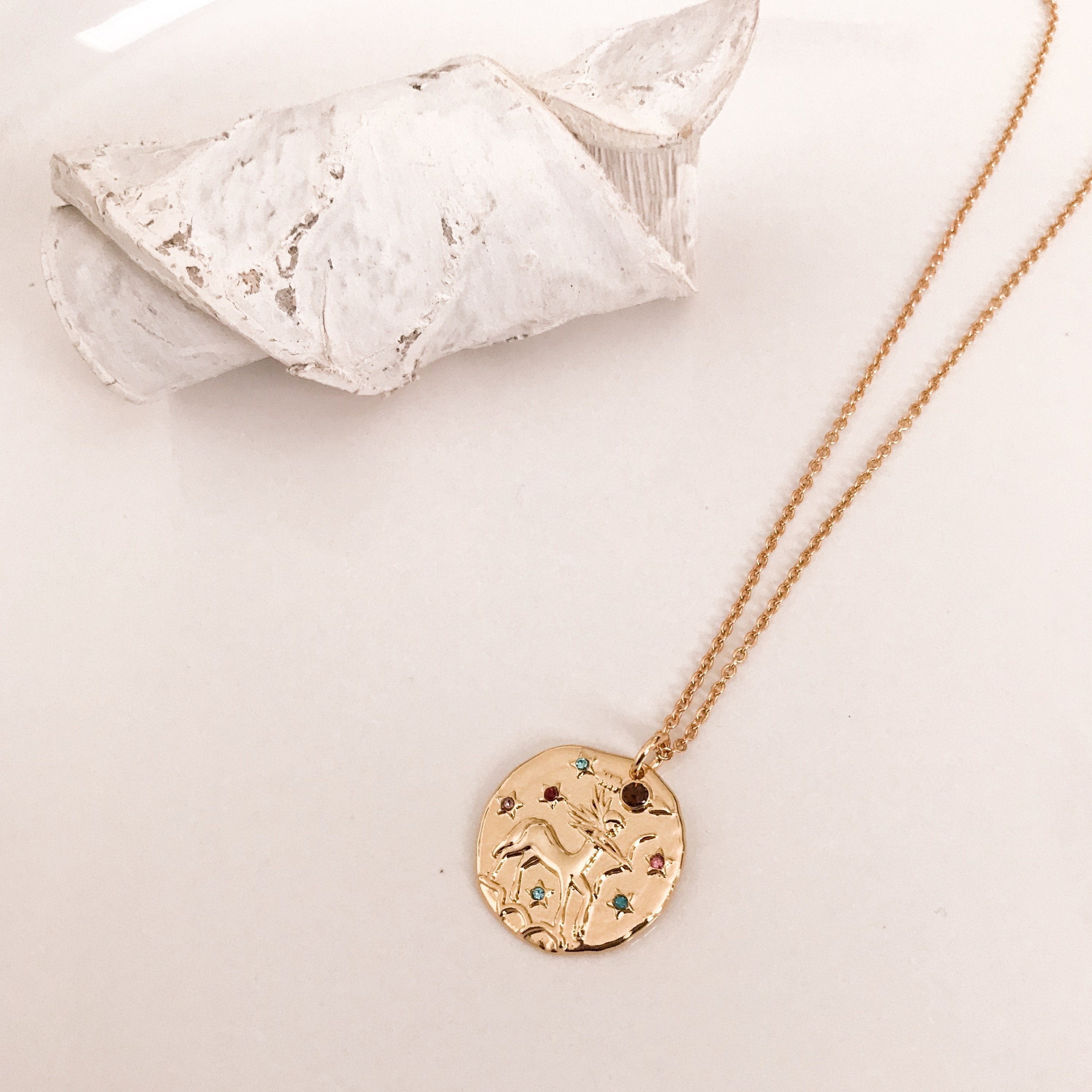 Discover our Wanderlust Zodiac Necklace collection, featuring exquisite hanging gold pendants with intricate designs on delicate chains. Some necklaces are embellished with vibrant gemstones. Crafted with hypoallergenic 18K gold plating, these pieces effortlessly combine elegance and comfort for everyday wear.
