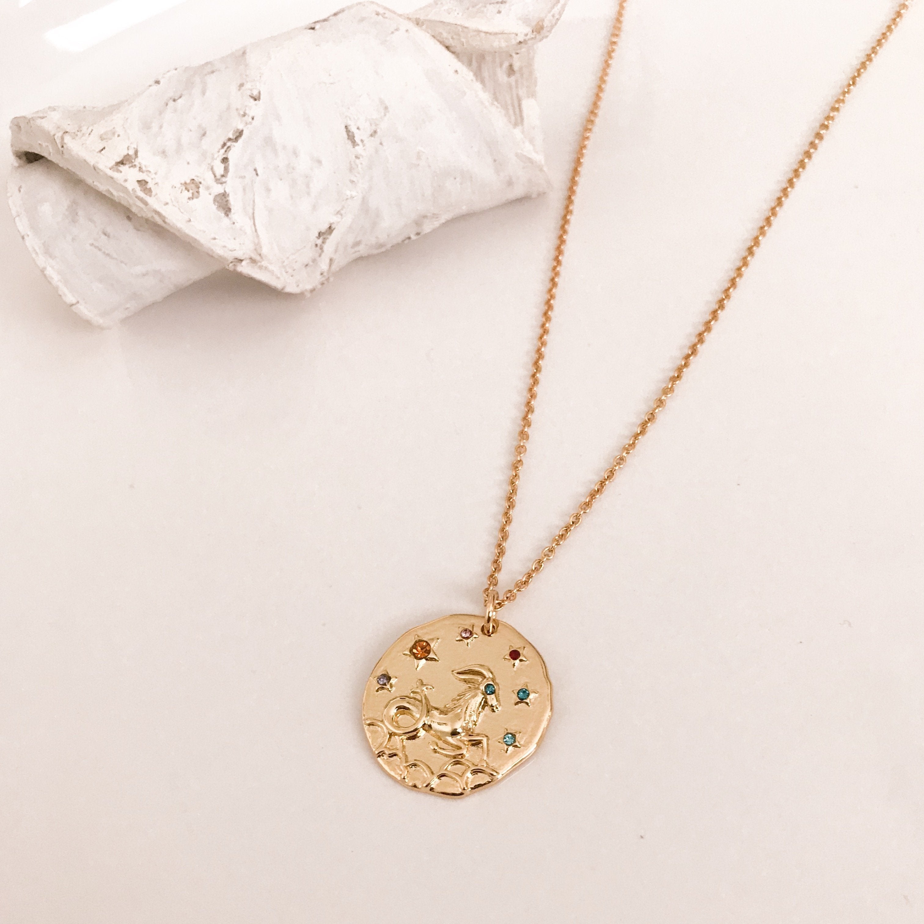 Discover our Wanderlust Zodiac Necklace collection, featuring exquisite hanging gold pendants with intricate designs on delicate chains. Some necklaces are embellished with vibrant gemstones. Crafted with hypoallergenic 18K gold plating, these pieces effortlessly combine elegance and comfort for everyday wear.