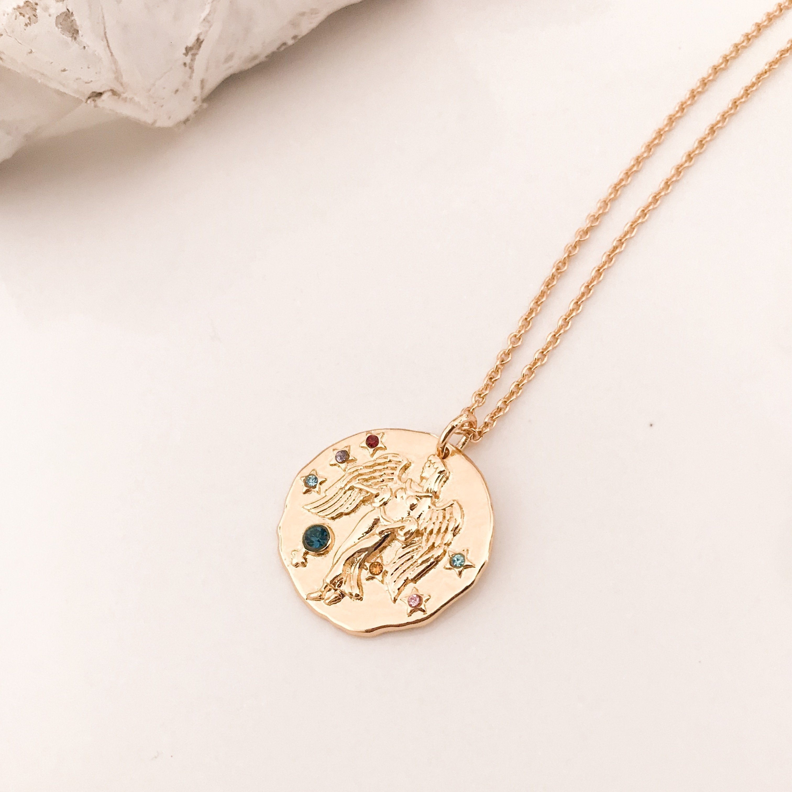 Discover our Wanderlust Zodiac Necklace collection, featuring exquisite hanging gold pendants with intricate designs on delicate chains. Some necklaces are embellished with vibrant gemstones. Crafted with hypoallergenic 18K gold plating, these pieces effortlessly combine elegance and comfort for everyday wear.