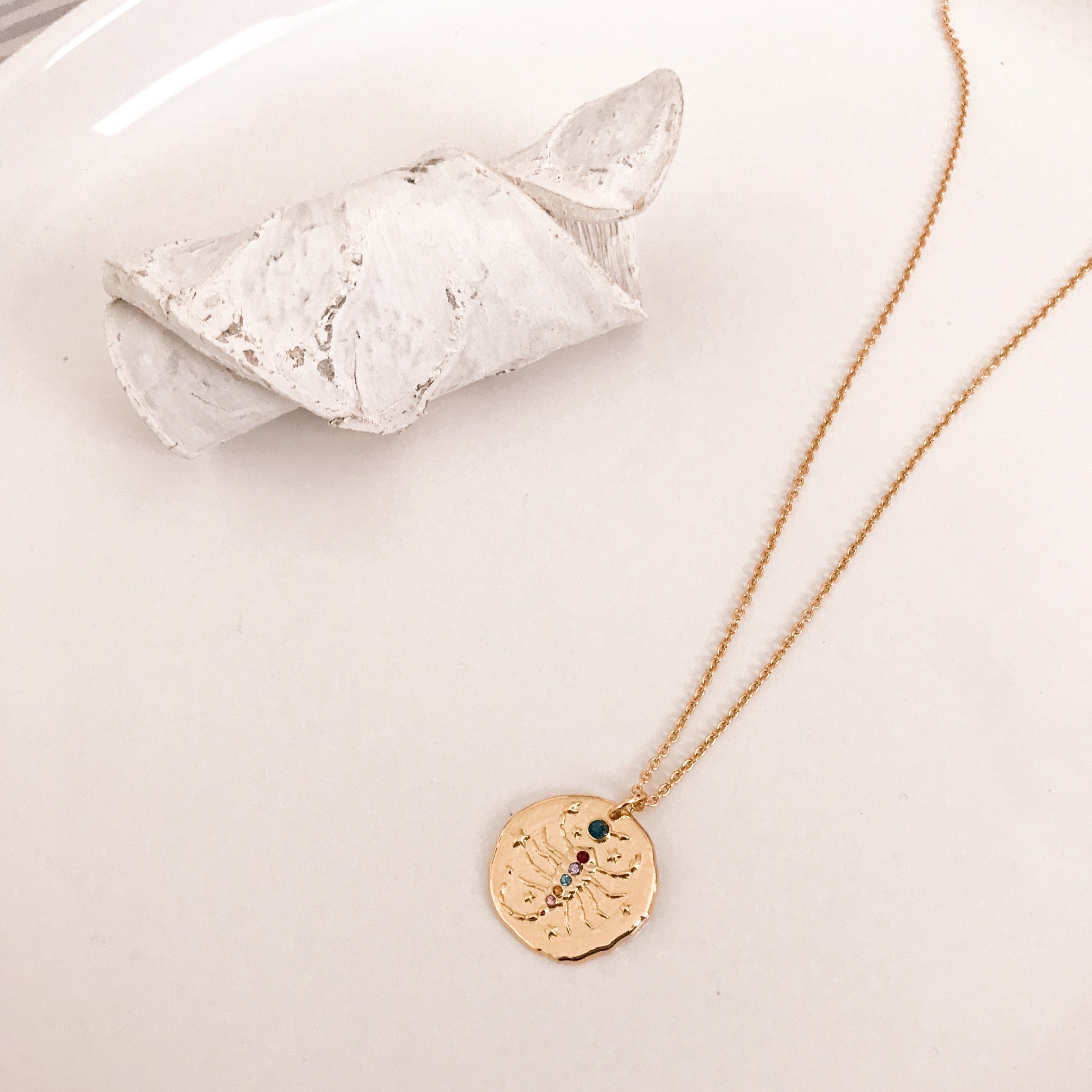 Discover our Wanderlust Zodiac Necklace collection, featuring exquisite hanging gold pendants with intricate designs on delicate chains. Some necklaces are embellished with vibrant gemstones. Crafted with hypoallergenic 18K gold plating, these pieces effortlessly combine elegance and comfort for everyday wear.
