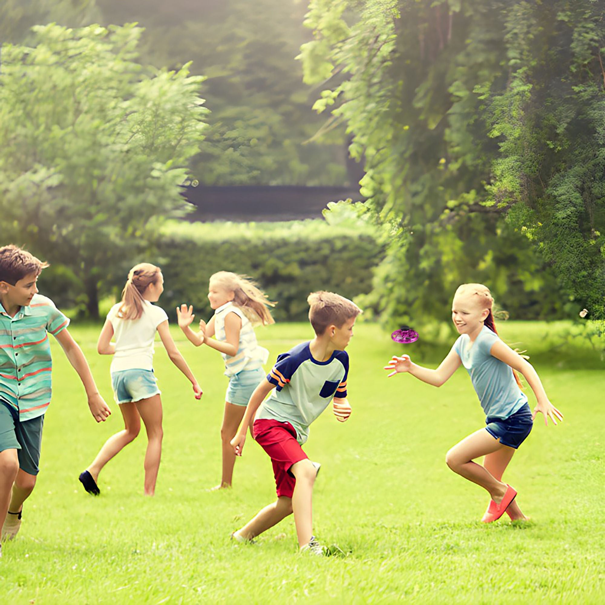 Children playing tag in a lush green park, with one girl in blue shorts reaching to tag a boy in a striped shirt, while a Glow Drone 360 Flying Toy with LED lights hovers above.