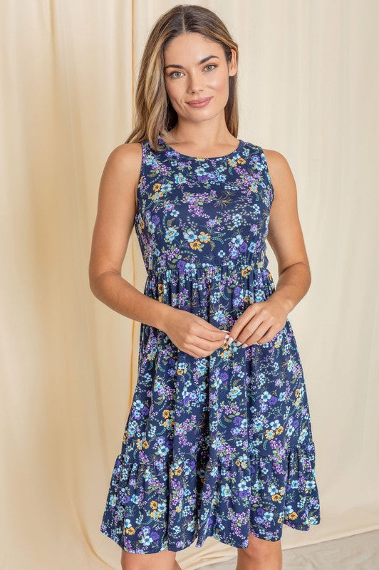 A woman in a Sleeveless Botanical Floral Tiered Dress and black sandals stands elegantly in front of a pink curtain.