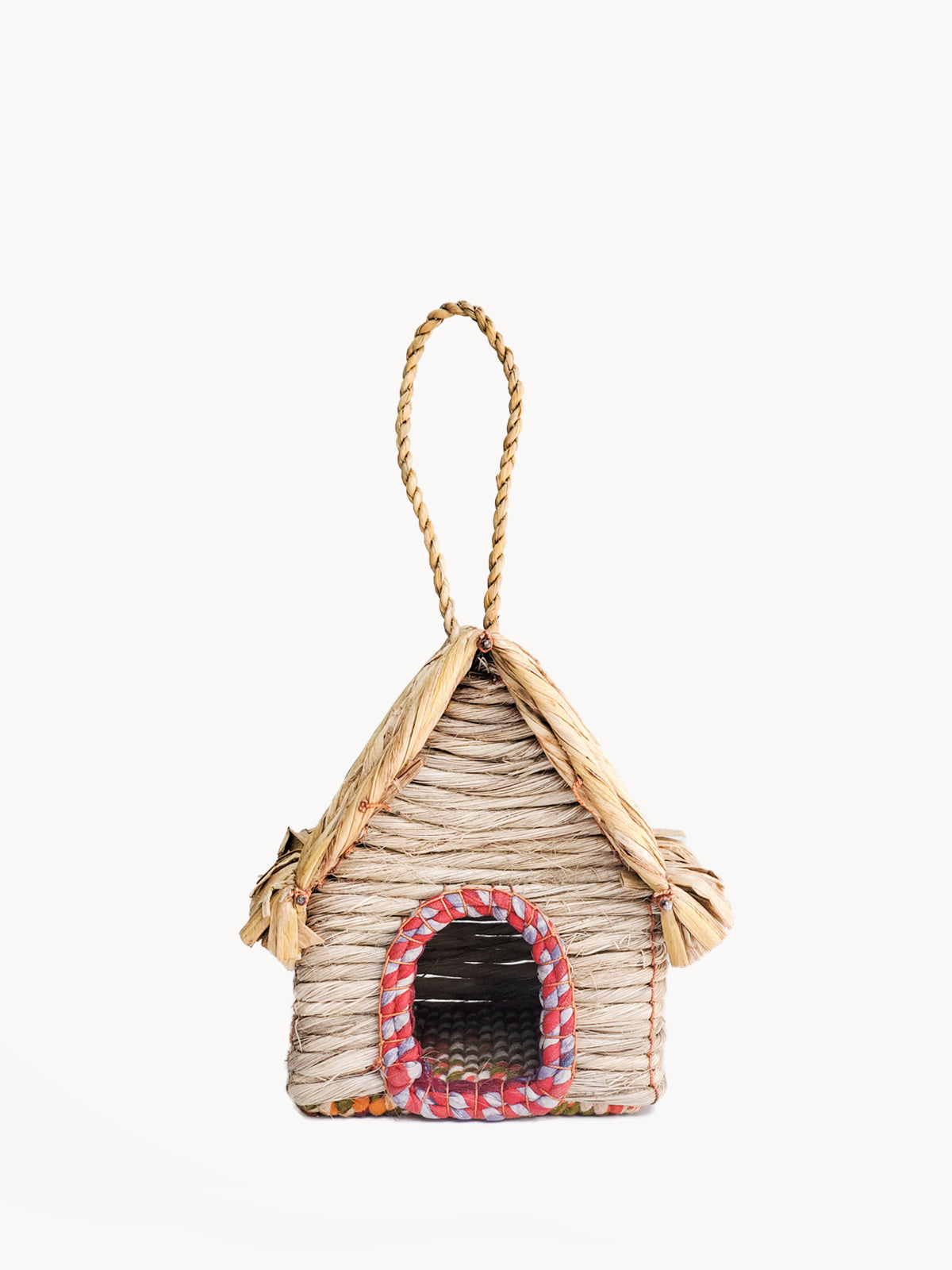 The Seagrass & Sari Birdhouse - Cabin, expertly handcrafted by Fair Trade artisans, features a red-trimmed entrance and a looped rope handle on top, all made from natural materials.