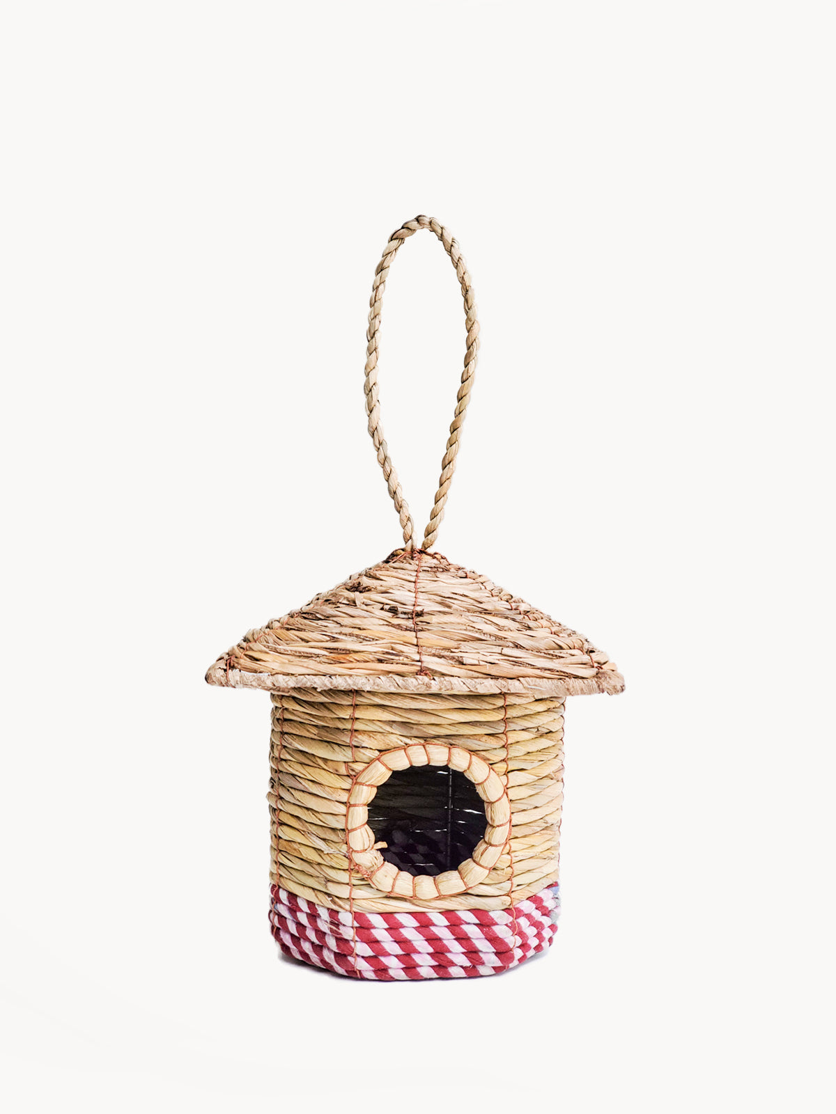 The Seagrass & Sari Birdhouse - Cottage is a handcrafted nest featuring a circular entrance, a red-and-white checkered base, and hangs by a rope loop, making it an environmentally friendly addition to your garden.