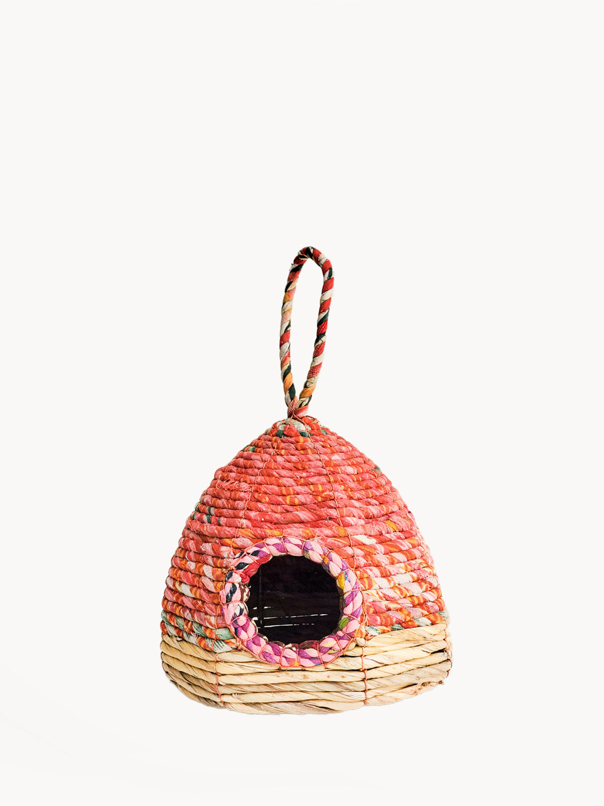 The Seagrass & Sari Birdhouse - Garden is an eco-friendly, handcrafted birdhouse showcasing a woven red and beige design, featuring a circular entrance and a looped handle on top.