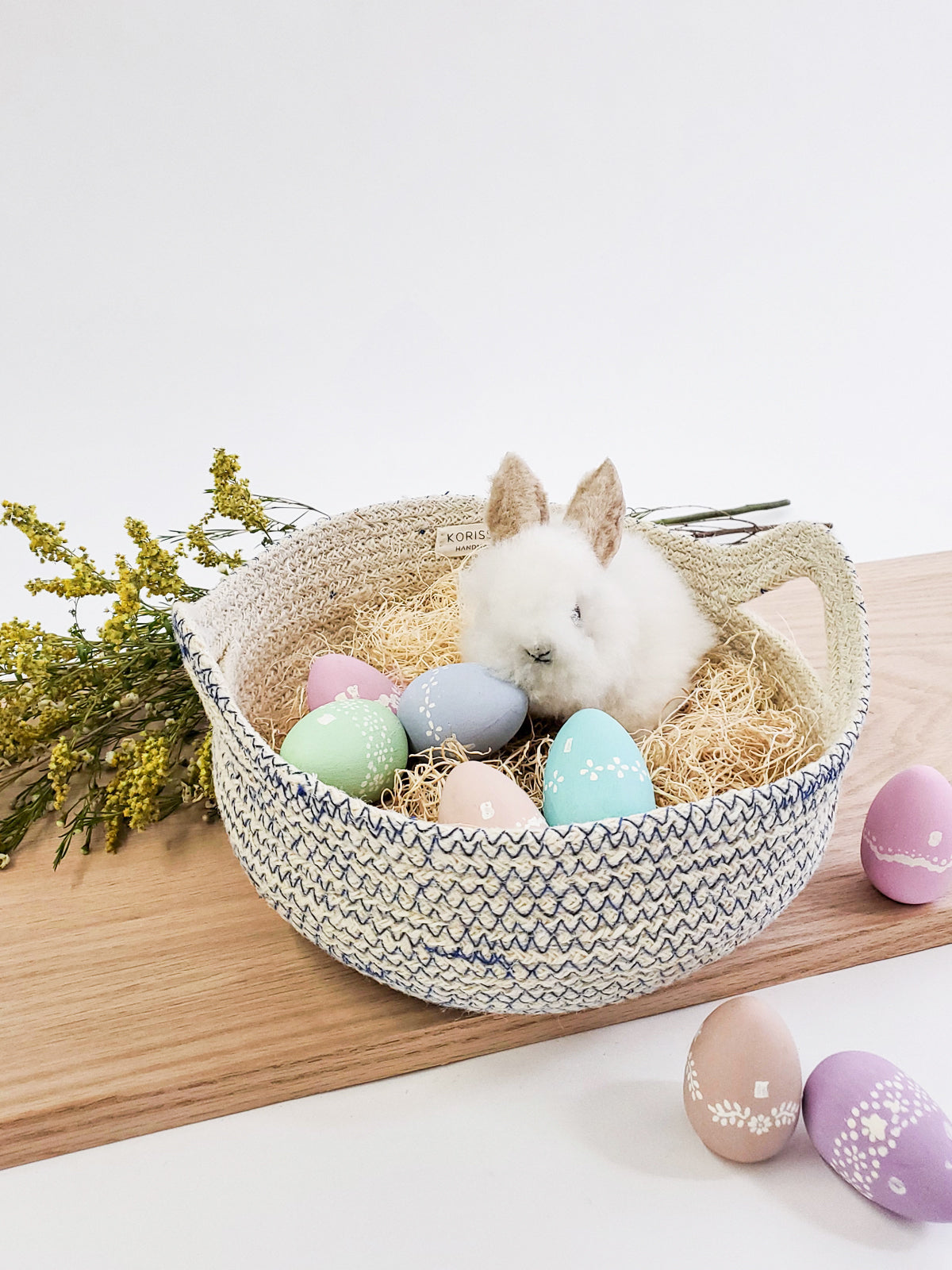 The Amari Fruit Bowl - Blue, handwoven by Fair Trade artisans, is artfully arranged on a plain background. Crafted sustainably with side handles, these baskets in varying sizes offer both beauty and functionality.