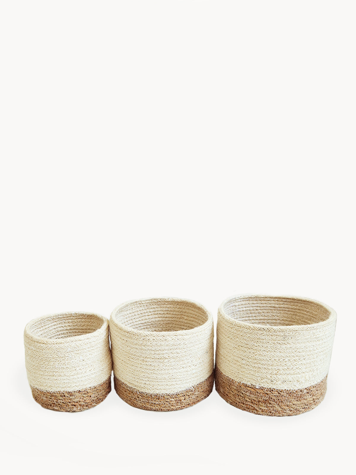 Three Savar Bins, woven sustainably by Fair Trade artisans in varying sizes, each featuring a beige upper half and a brown lower half, are arranged in a row.