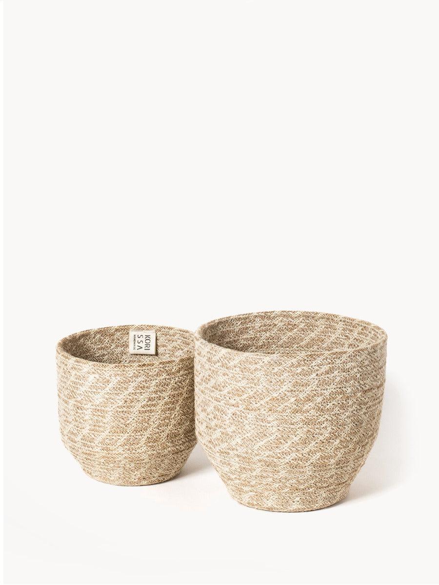 The Agora Bin set includes two woven baskets of different sizes, meticulously handmade from natural fibers. These exquisite pieces are adorned with jute yarn detailing and embody fair trade principles.