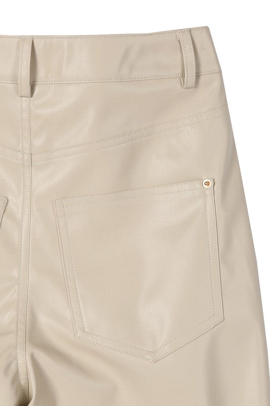 A person wearing a white sweater and black Vegan leather pants with hands in the pockets.