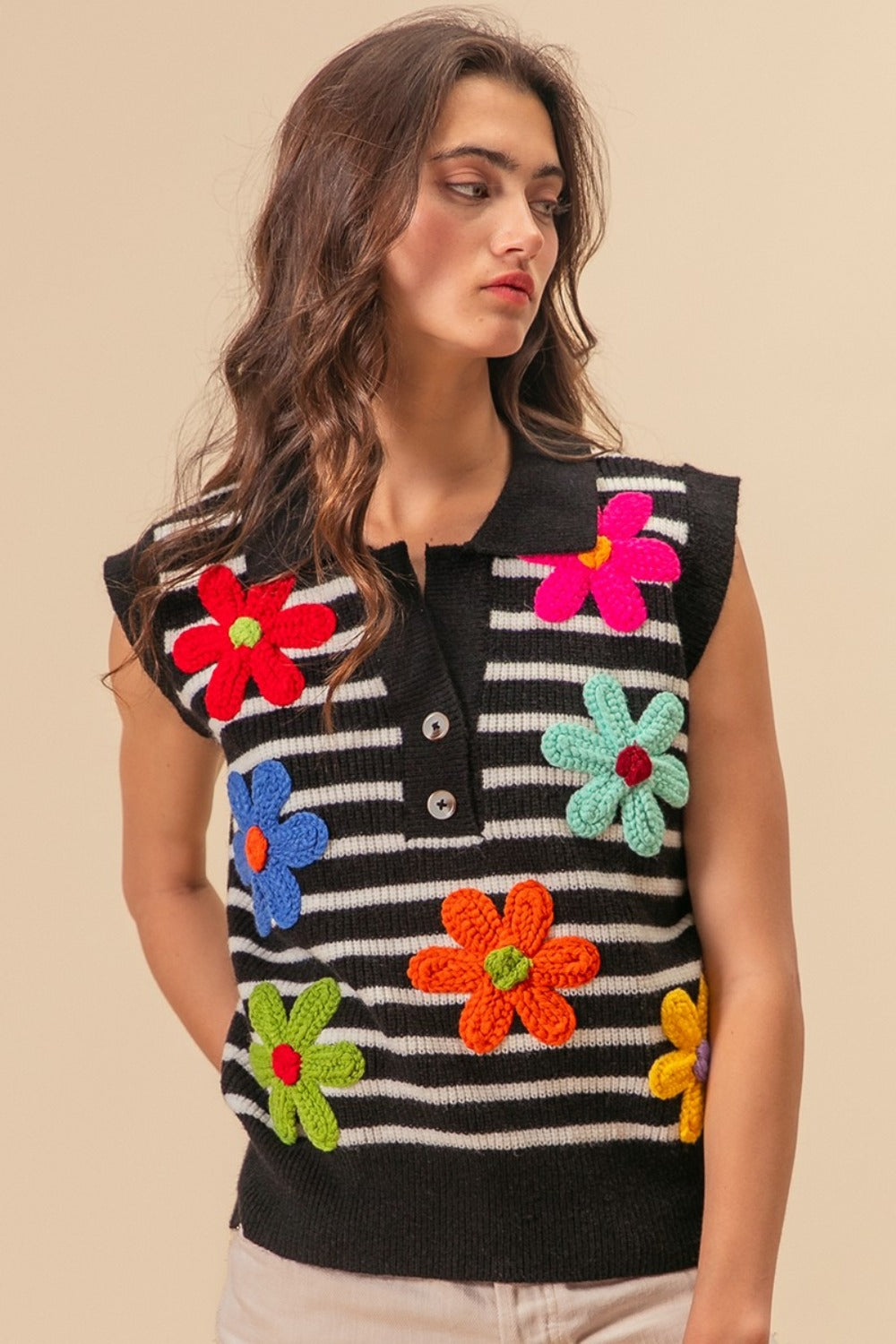 A person wearing the BiBi Flower Patch Striped Half Button Sweater Vest, a sleeveless top featuring black and white stripes adorned with colorful floral patches.