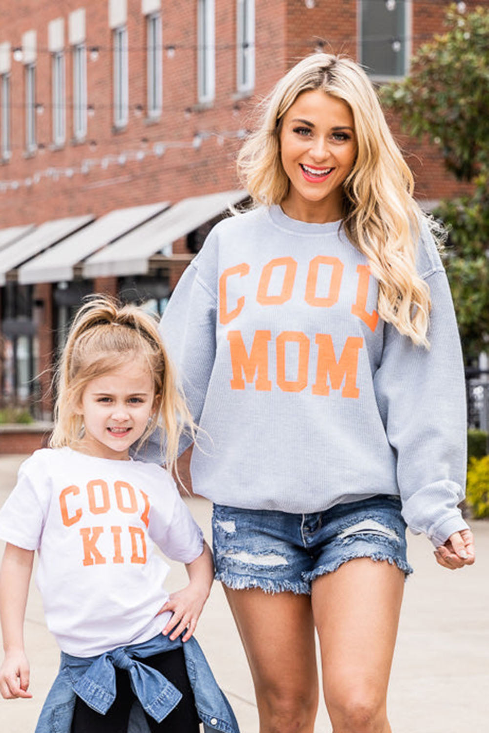 A person with long blonde hair stands facing away, wearing a Gray Cool Mom Graphic Print Cording Sweatshirt and blue jeans.