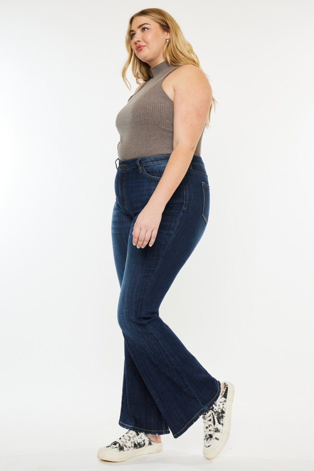 A person poses in a sleeveless brown top, Kancan Full Size Mid Rise Flare Jeans, and sneakers against a plain white background.