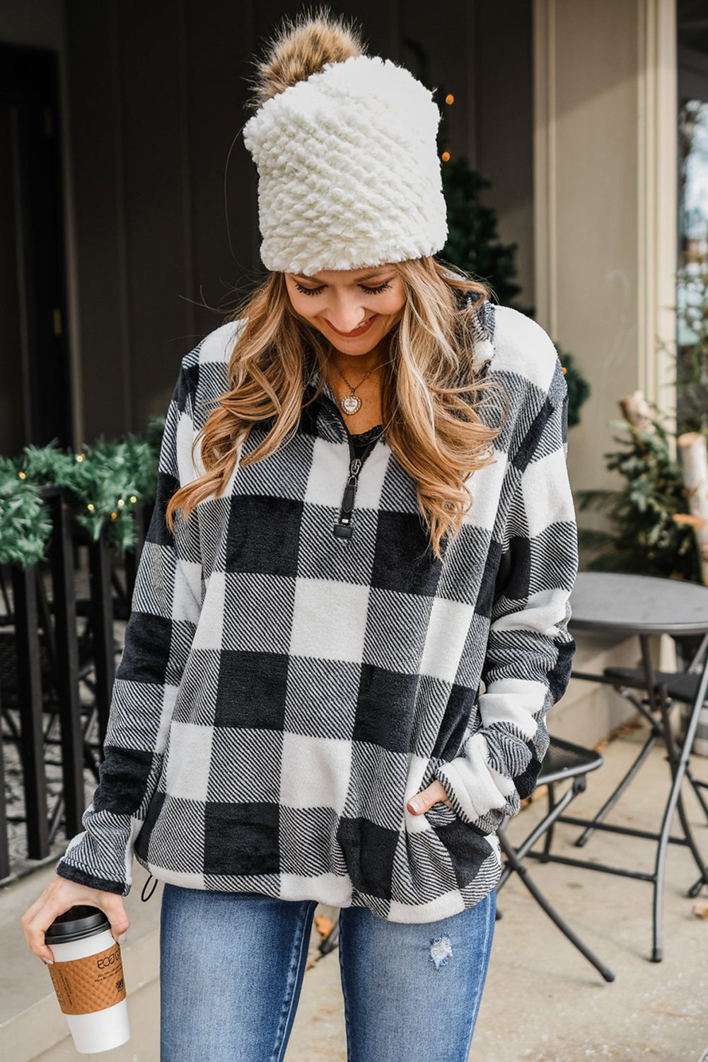 A woman with wavy hair is wearing a cozy Black Plaid Print 1/4 Zip Turn-down Collar Sweatshirt and blue jeans, standing with her back to the camera against a textured gray background.