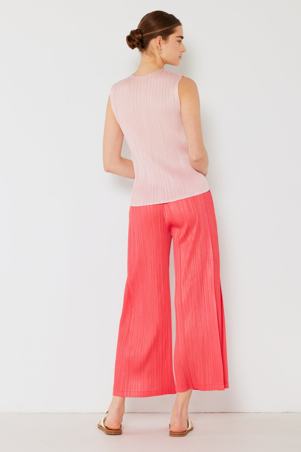 A person wearing the Marina West Swim Pleated Wide-Leg Pants with side pleat detail in red, standing against a white background with hands in pockets and wearing white sandals.