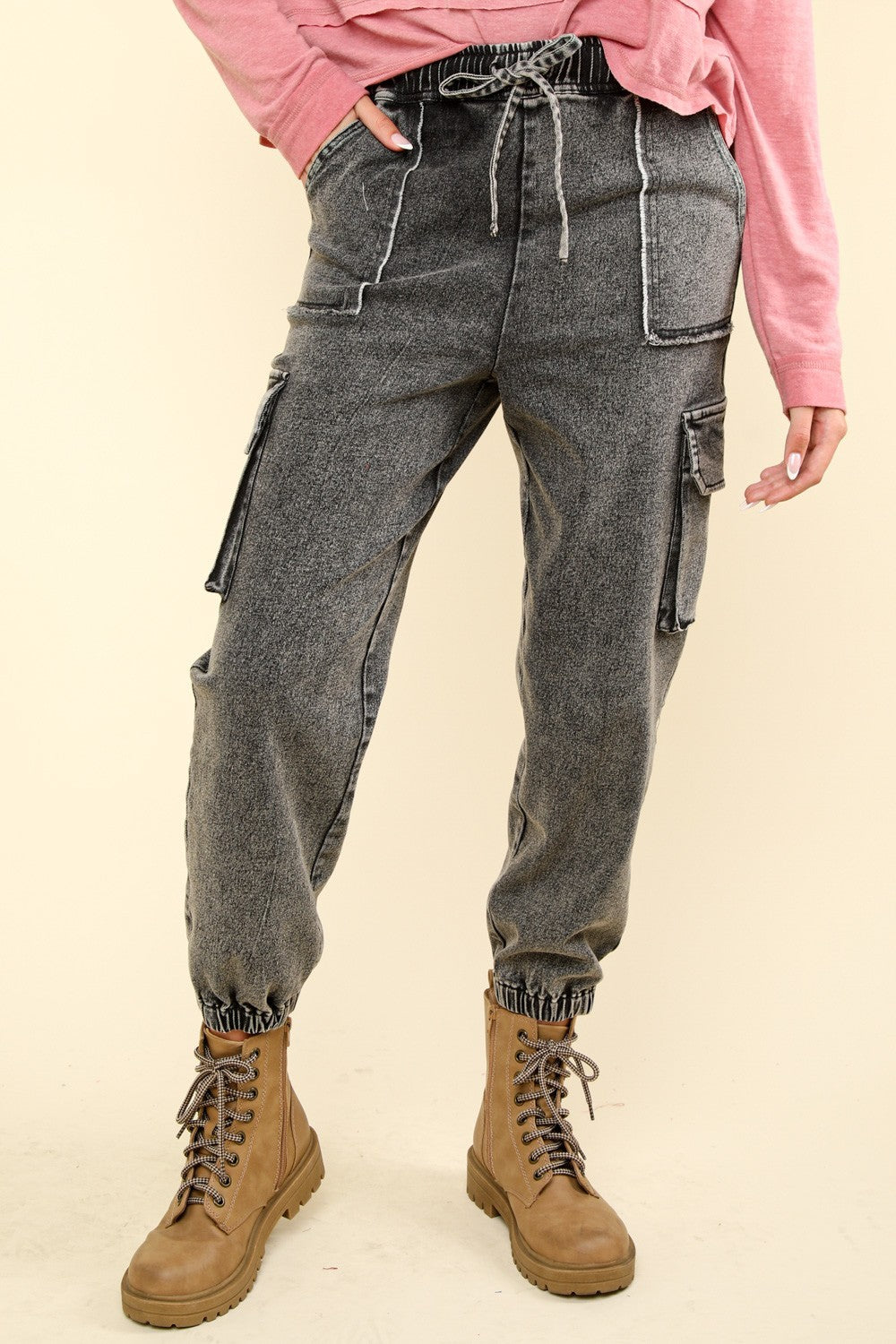 Person wearing VERY J Washed Drawstring Jogger Cargo Jeans with practical side pockets and tan lace-up boots, paired with a pink long-sleeve shirt.