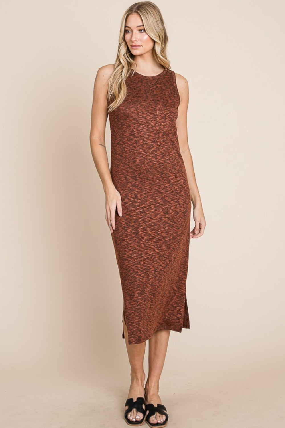 A woman with long blonde hair stands against a beige background, wearing the versatile and stylish BOMBOM Slit Round Neck Sleeveless Midi Dress in rust color, featuring a slit round neck and side slit, paired with black sandals.