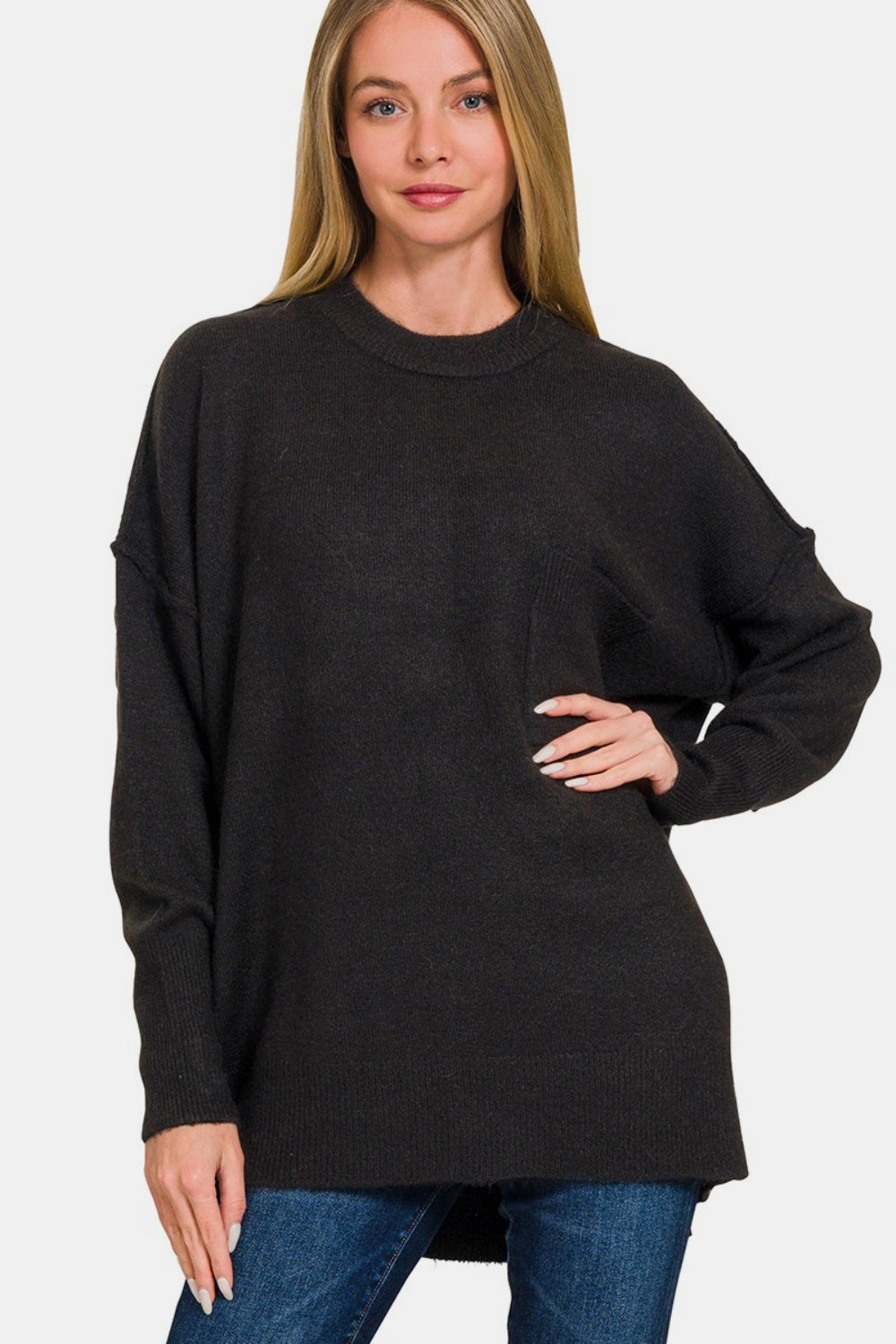 A person wearing the Zenana High-Low Hem Drop Shoulder Sweater, paired with jeans, poses elegantly against a plain background.