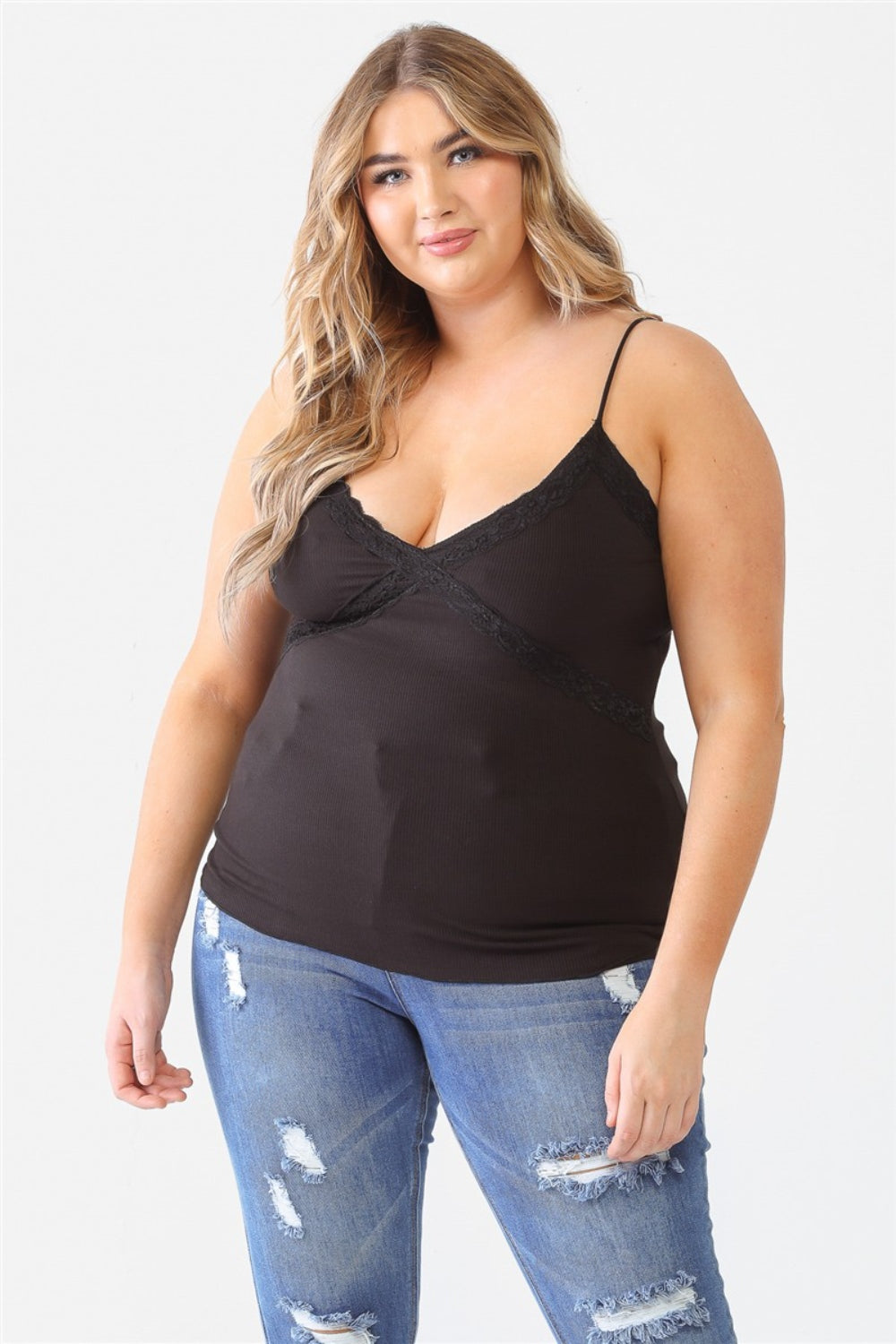 A person with long hair is wearing a Zenobia Plus Size Lace Detail V-Neck Cami and distressed jeans against a plain background.