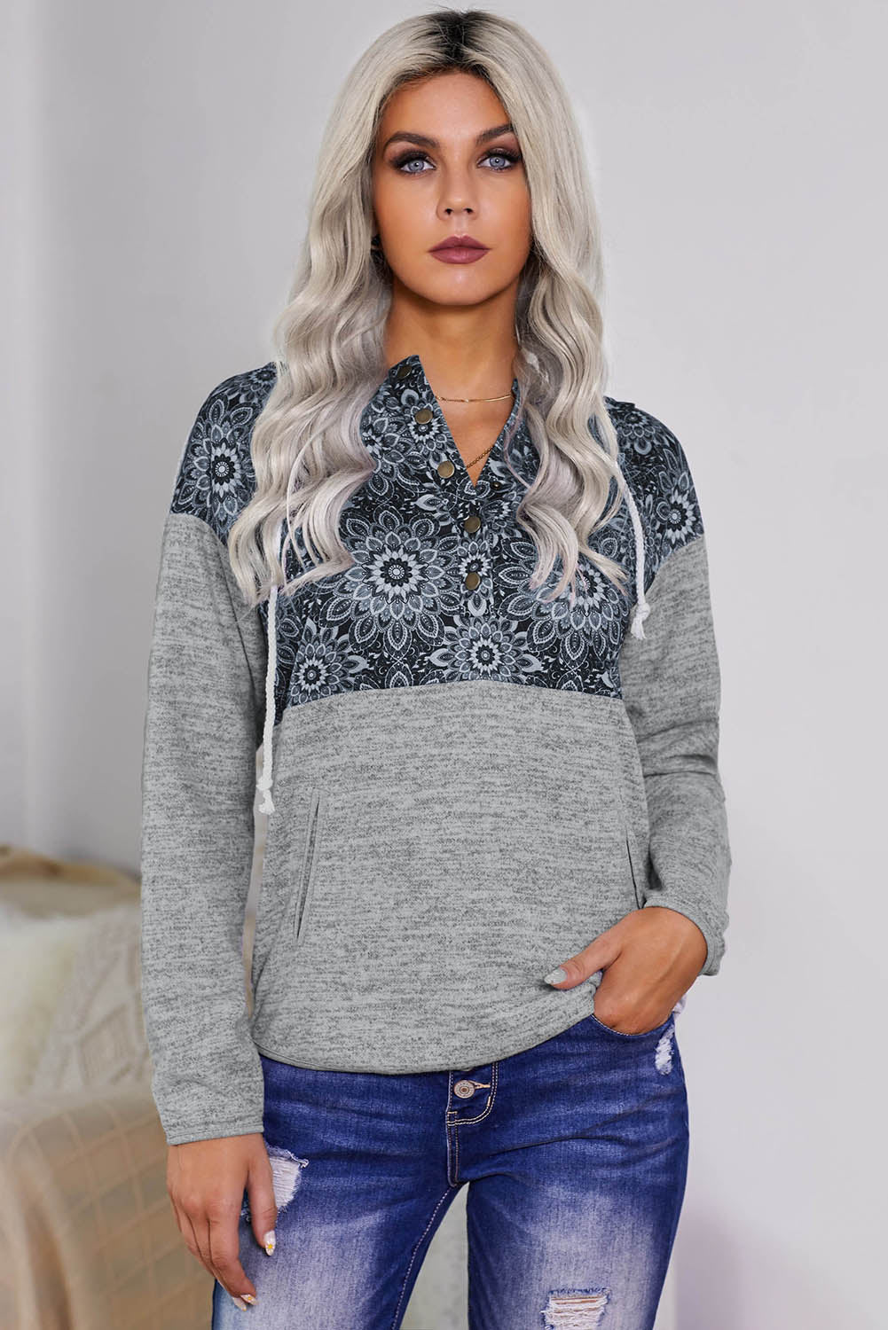 A person with long blonde hair is wearing a Gray Tribal Print Vintage Pocket Hoodie. They are turned sideways, and pampas grass in a vase is visible in the background.