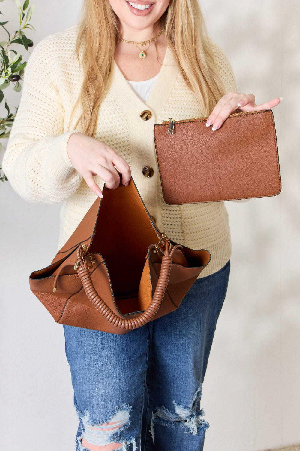 Effortlessly displaying the SHOMICO Faux Leather Handbag with Pouch, which features a spacious design in brown with gold accents and a woven handle, this piece exemplifies versatility. Paired with a cream sweater and blue jeans, its minimalist style perfectly balances fashion and function.