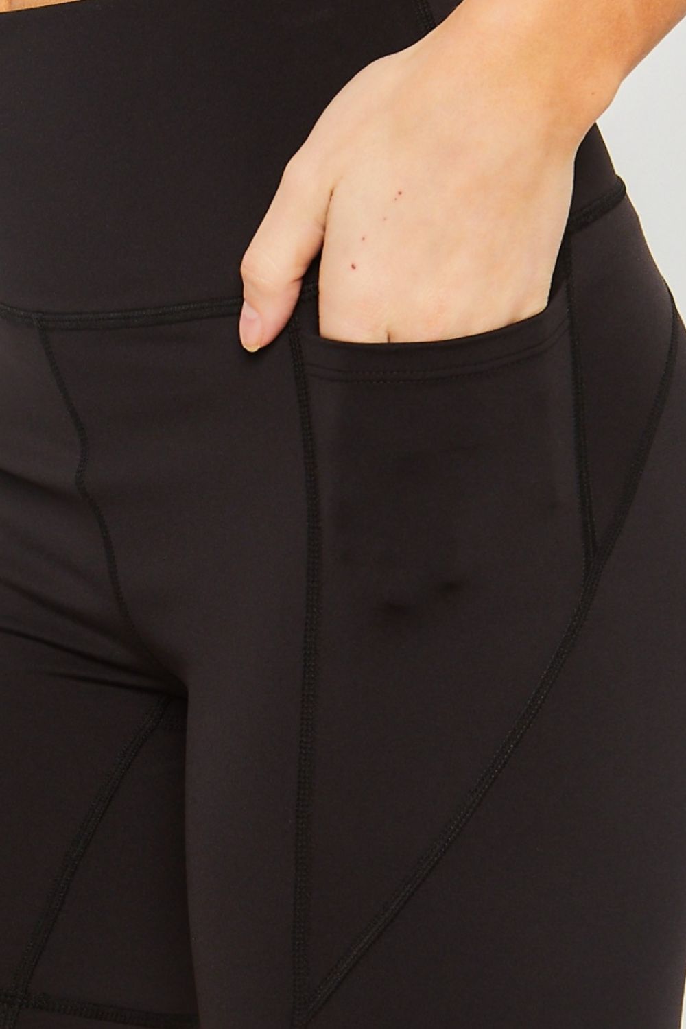 A person wearing Love Tree High Waist Seam Detail Active Shorts in black, casually resting their hands in the pockets against a plain background.