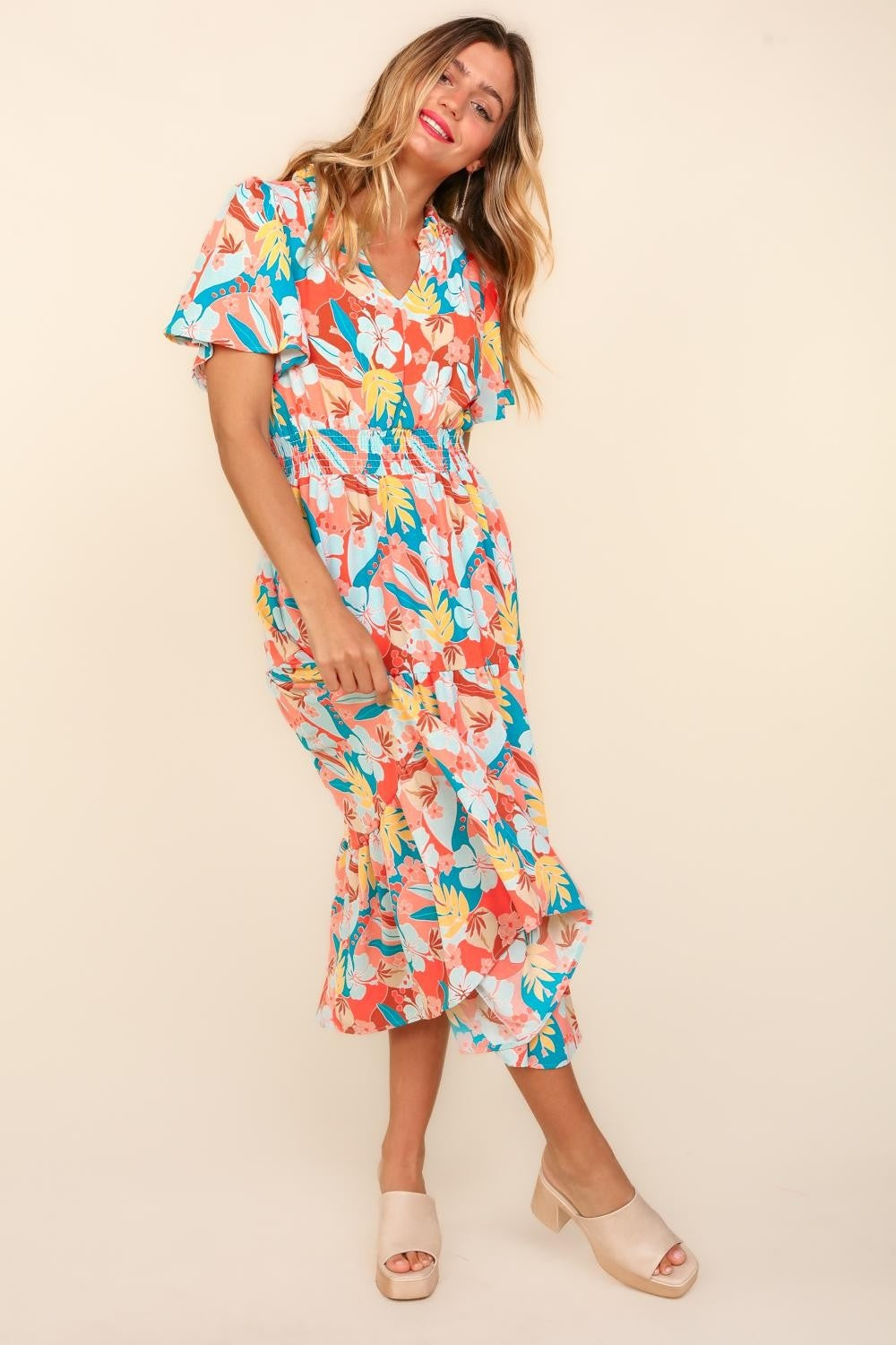 A person wearing the Haptics Full Size Tropical Floral Tiered Dress with Side Pockets and beige platform sandals stands against a plain background.