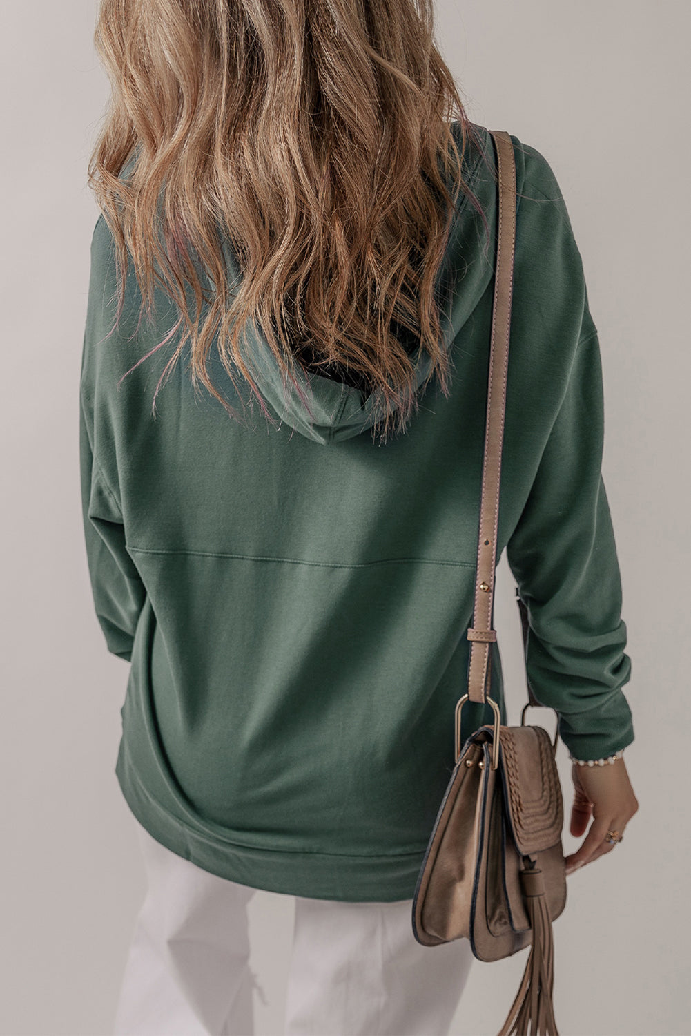 A person with long, wavy hair wearing a Sea Green Casual V Neck Drawstring Hoodie and white pants, carrying a brown crossbody bag. The person's back is facing the camera.