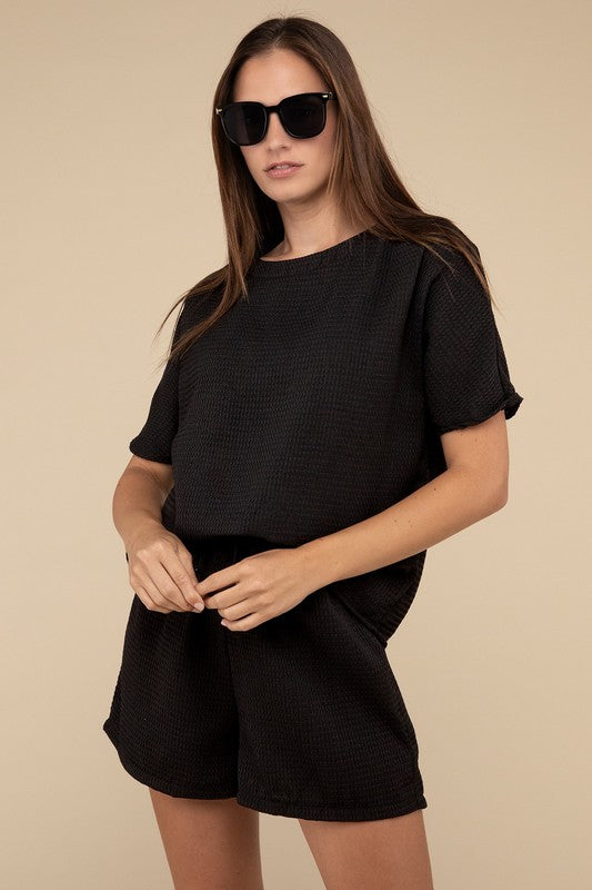 Clad in the Waffle Round Neck Top and Short Set paired with black sunglasses, a person stands against a plain beige background, highlighting the non-stretch polyester fabric.