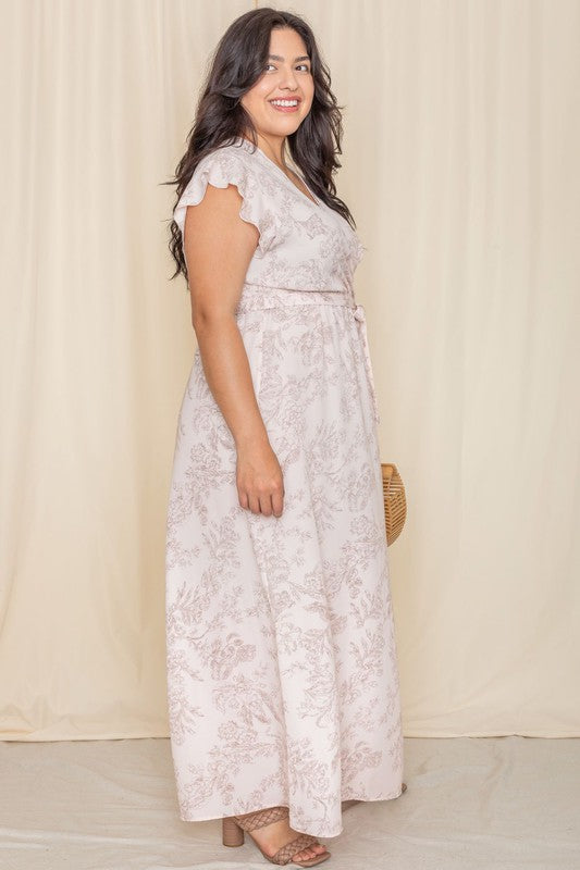 A woman wearing a Floral Surplice Sash Sundress, which is light yellow and unlined, stands smiling against a cream-colored background.