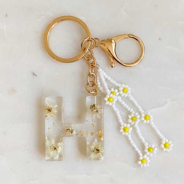 Baby Daisy Initial Key Chain alphabet keychains with real daisy flowers and gold flakes on a marble surface.