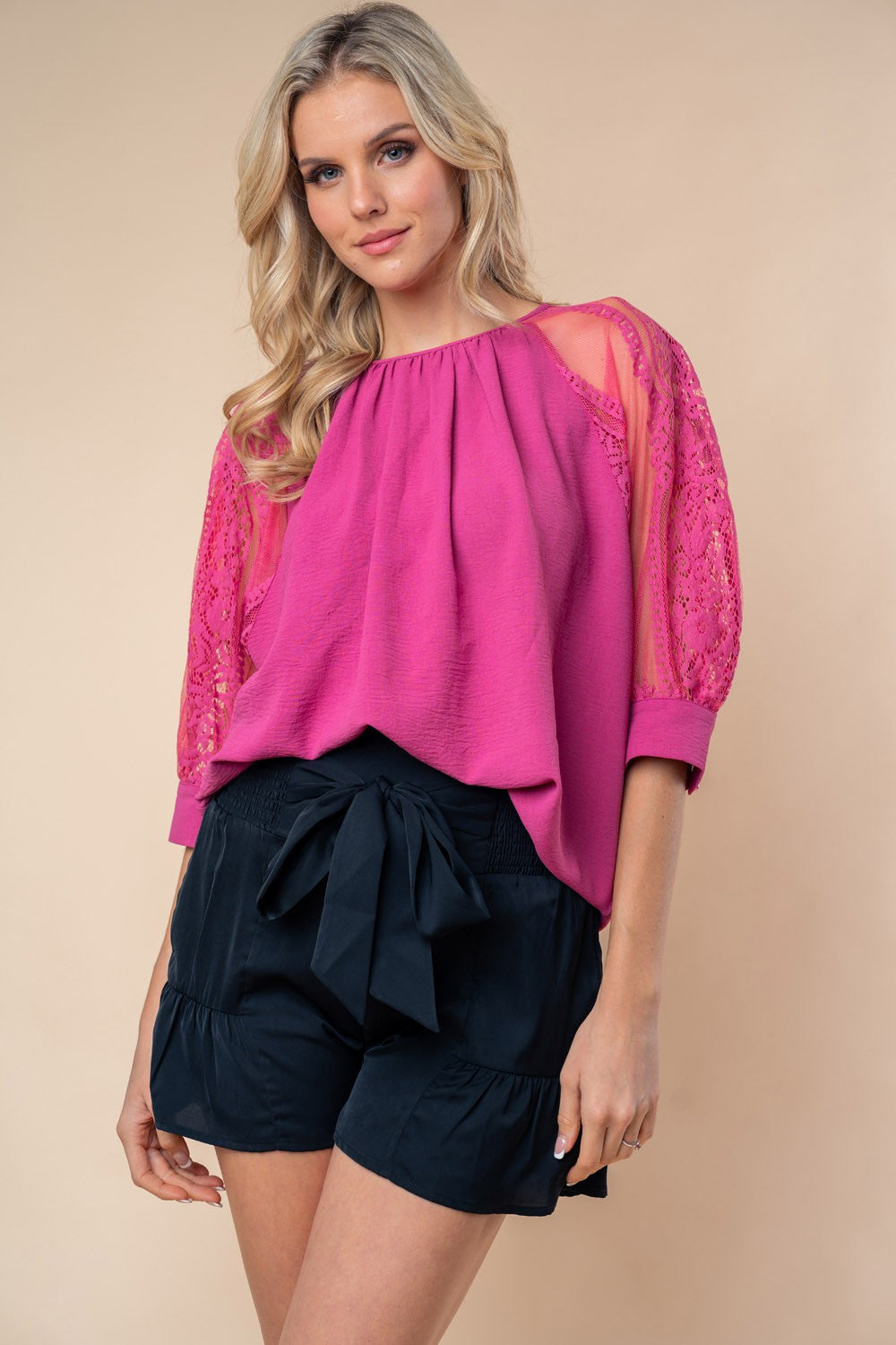 A person stands against a neutral background, wearing the White Birch round neck blouse with vibrant pink lace half sleeves.