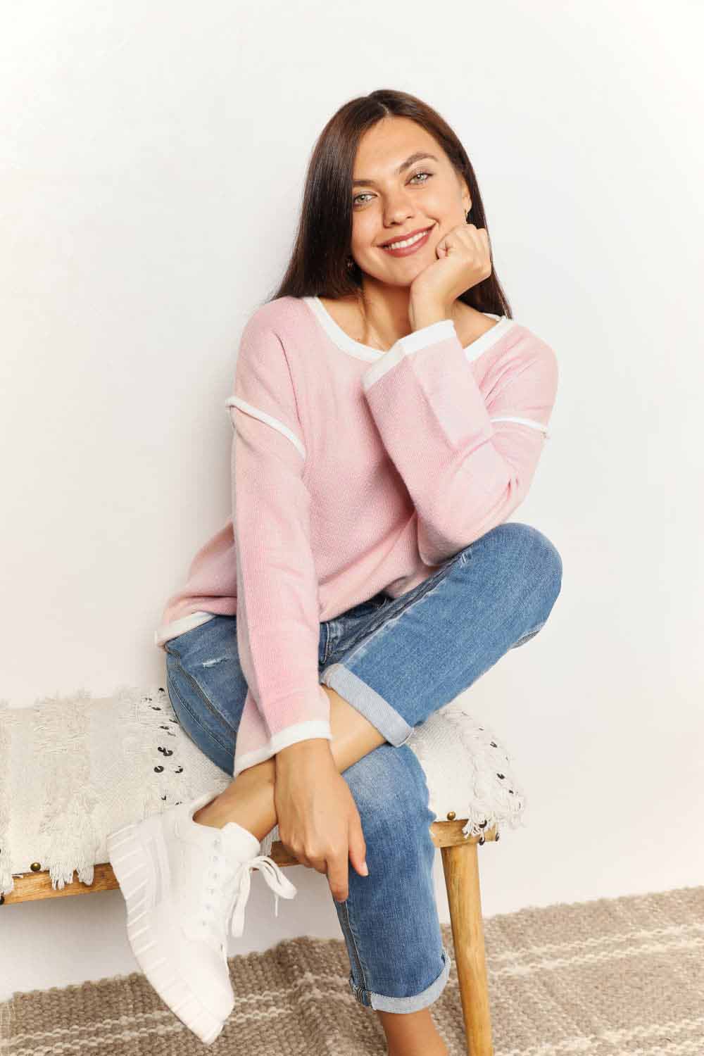 A woman with long curly hair is wearing the Angel Wings Contrast Detail Dropped Shoulder Knit Top in pink, paired with blue jeans, standing against a light background.