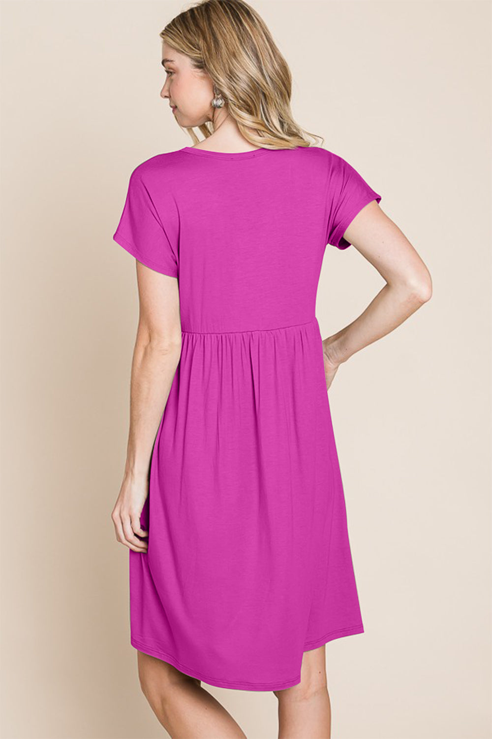 A person stands against a neutral background wearing the BOMBOM V-Neck Short Sleeve Dress, featuring a vibrant pink color and button details, crafted from soft rayon spandex fabric.