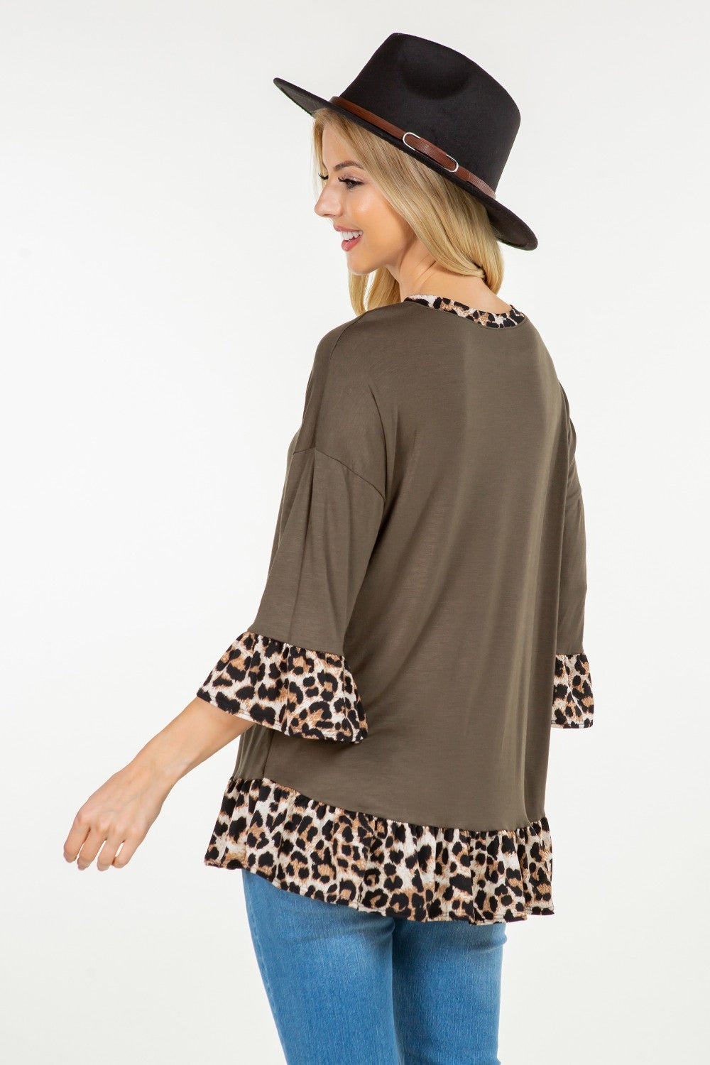 Person wearing the Celeste Full Size Flounce Sleeve Leopard Trim Top in brown, paired with blue jeans and a black hat, posing elegantly against a plain background.