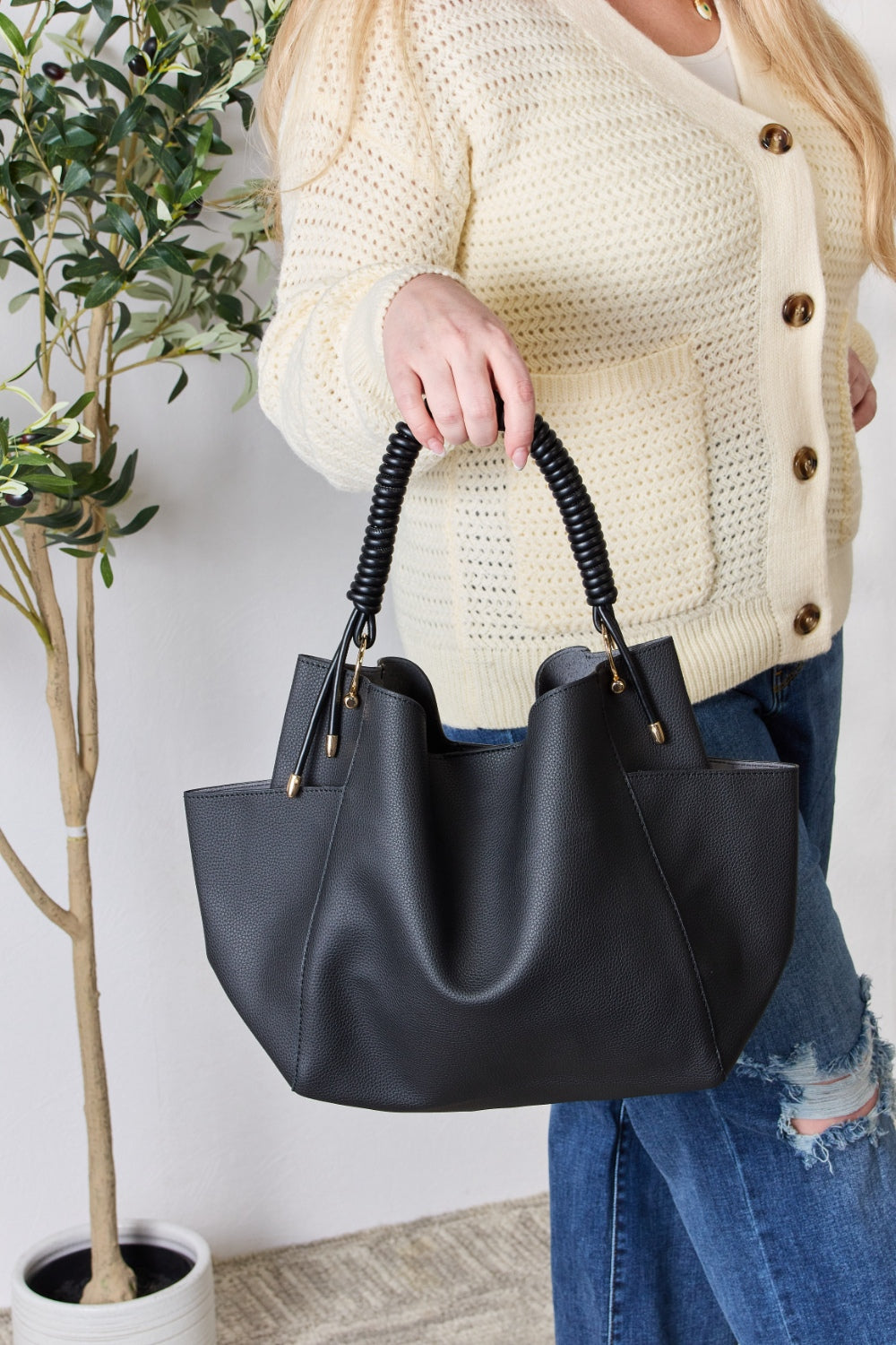 Effortlessly displaying the SHOMICO Faux Leather Handbag with Pouch, which features a spacious design in brown with gold accents and a woven handle, this piece exemplifies versatility. Paired with a cream sweater and blue jeans, its minimalist style perfectly balances fashion and function.