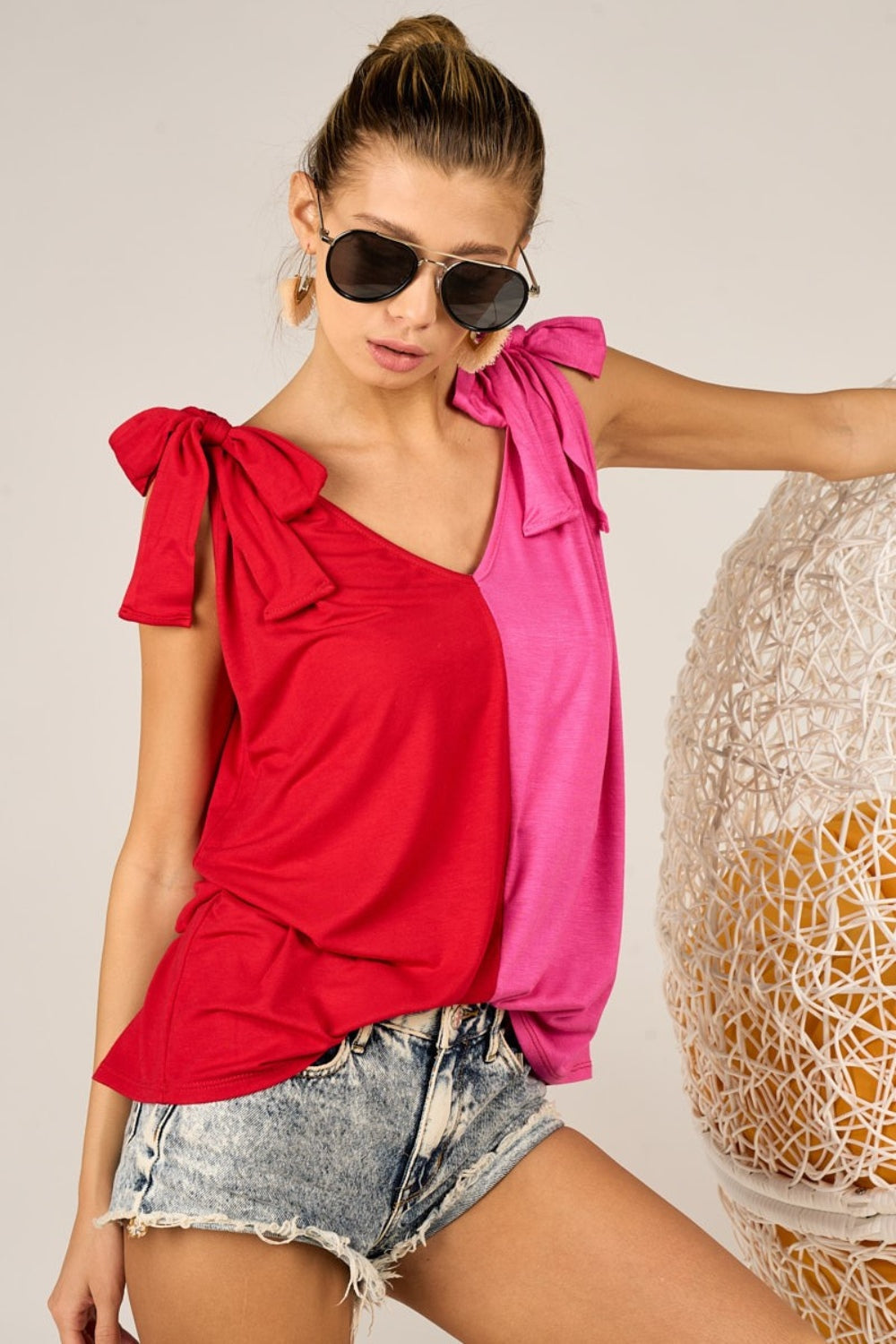 A person wearing the stylish BiBi Shoulder Ribbon Tied Contrast Tank, paired with denim shorts, sunglasses, and earrings, poses against a neutral background.