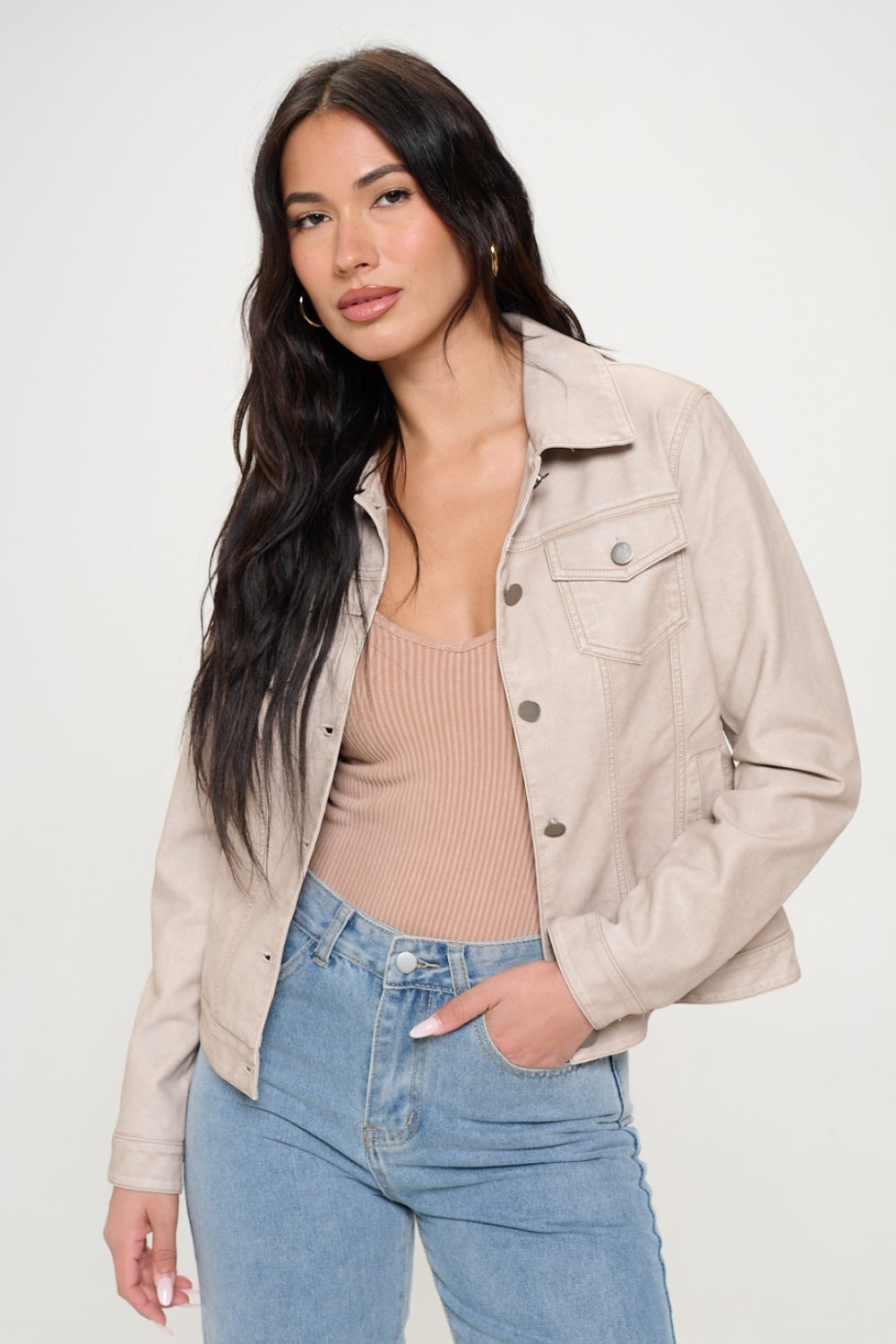 A woman with long dark hair, showcasing women's spring fashion, wears the Coalition LA Button Down Cargo Vegan Leather Shacket over a beige top and blue jeans as she stands against a plain background.