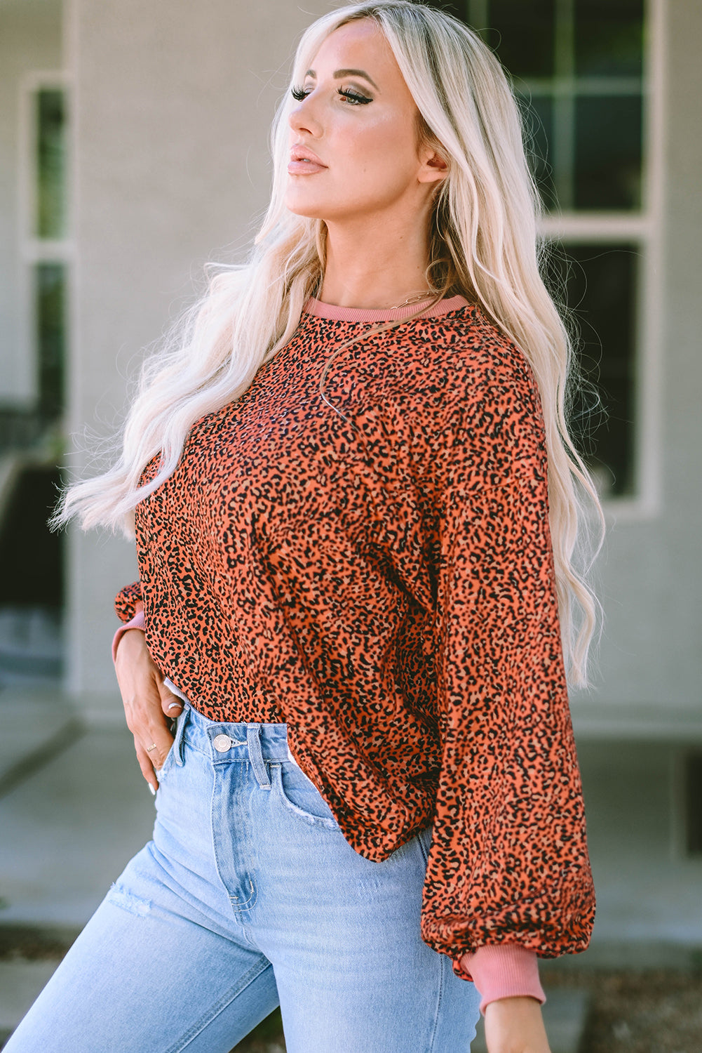 A person with long blonde hair is facing away, wearing a red and black patterned top and light blue jeans. Their right hand is resting on their hip, reminiscent of the casual charm captured by the Vintage Leopard Bubble Sleeve Pullover Sweatshirt.