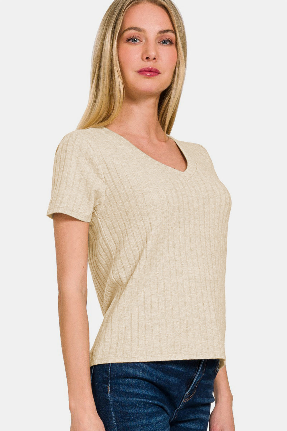 A woman with long blonde hair wears a cream-colored Zenana Ribbed Short Sleeve T-Shirt made from high-quality materials and dark jeans, posing against a plain background.