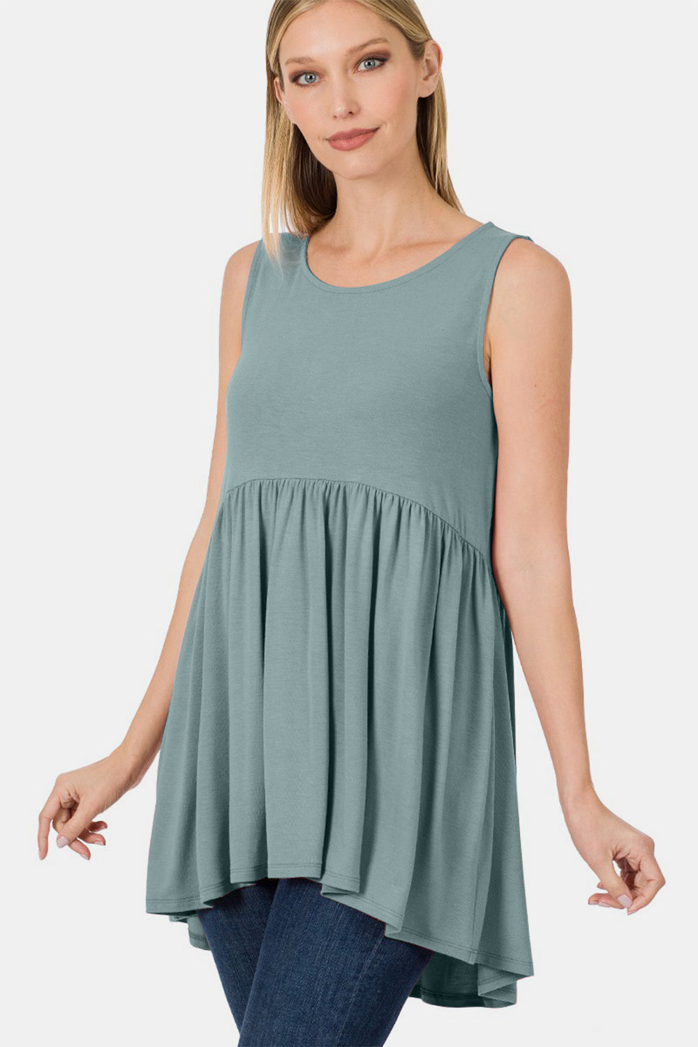 A person wearing a Zenana Round Neck Wide Strap Babydoll Top in light green with blue jeans stands while smiling.