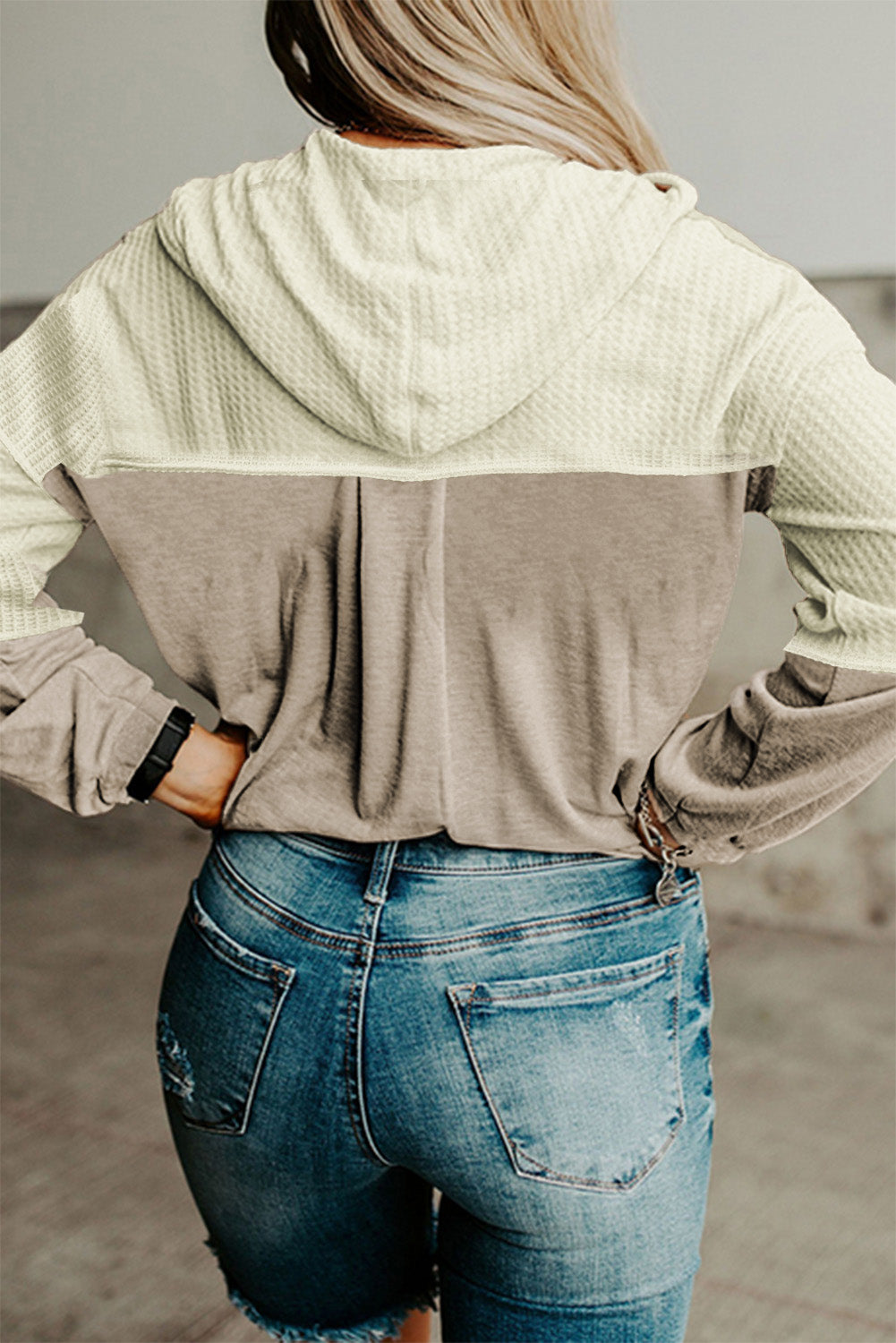 A person with long hair is seen from the back wearing an Apricot Contrast Block Waffle Knit Hoodie in cream and gray, paired with distressed denim jeans.