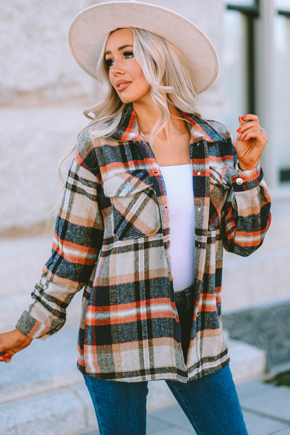 A person wearing a Brown Plaid Button Up Long Sleeve Flannel Shacket layered over a white top with ripped jeans and holding a brown handbag stands against a textured gray wall.