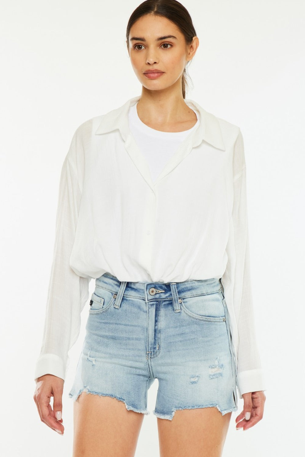 A person wearing a white shirt and the chic Kancan High Rise Side Slit Denim Shorts stands against a plain background, showcasing a perfect addition to any summer wardrobe.